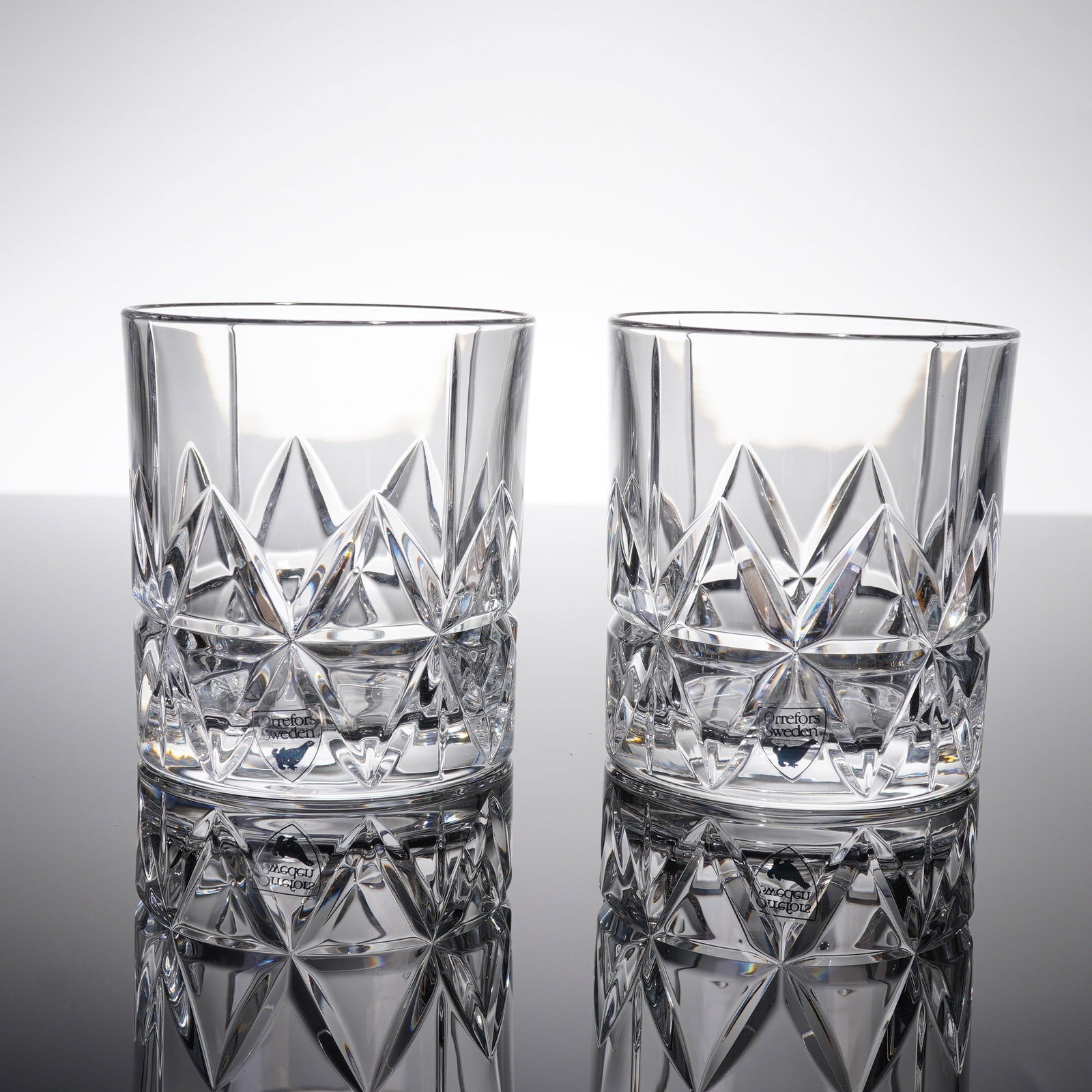 A Pair of Orrefors Peak Double Old Fashioned Crystal Glasses: A pair of Orrefors Peak Double Old Fashioned tumblers, crafted from clear crystal. These heavy cylindrical whiskey glasses feature deeply faceted traditional diamond-cut paterning encircling the lower