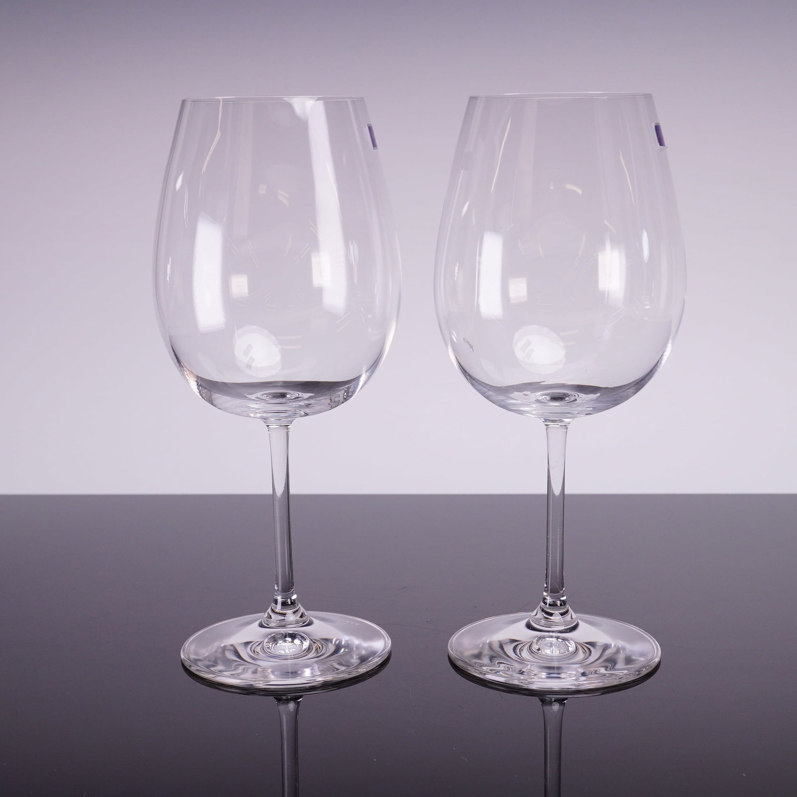 Pair of Marquis by Waterford Crystal Bordeaux Wine Glasses: A pair of modern crystal stemmed wine glasses manufactured by Marquis by Waterford. These glasses feature large, clear bowls suitable for Bordeaux or Cabernet style red wines, supported by thin stems 