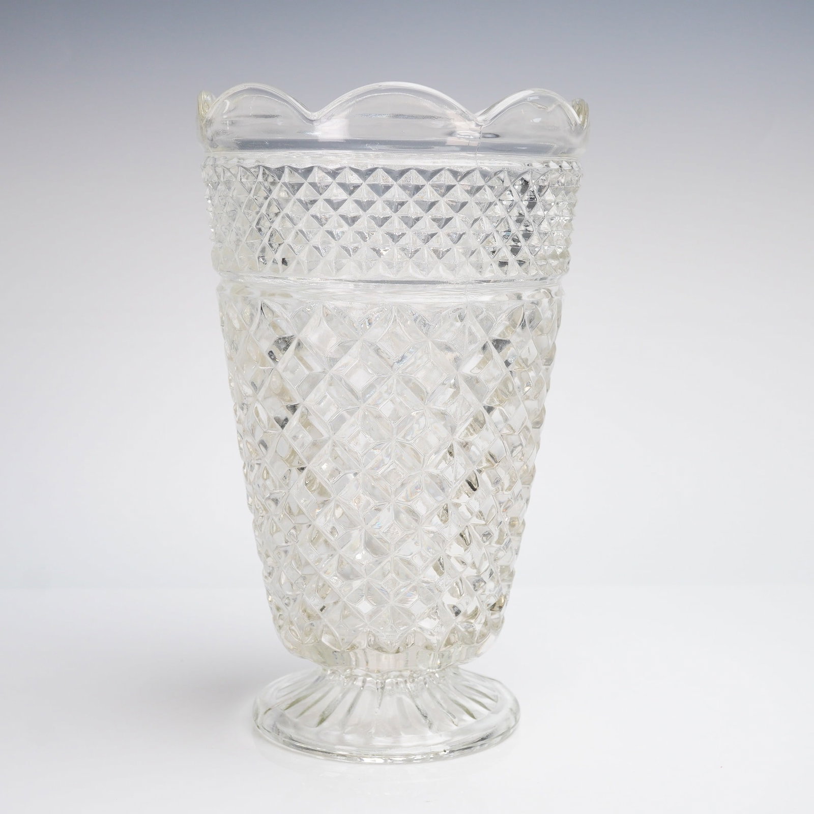 Anchor Hocking Wexford Pattern Clear Glass Footed Vase: A clear pressed glass vase in the highly recognizable Wexford pattern manufactured by Anchor Hocking. This footed glass vase features a tapered cylindrical body resting on a short, spreading pedestal 