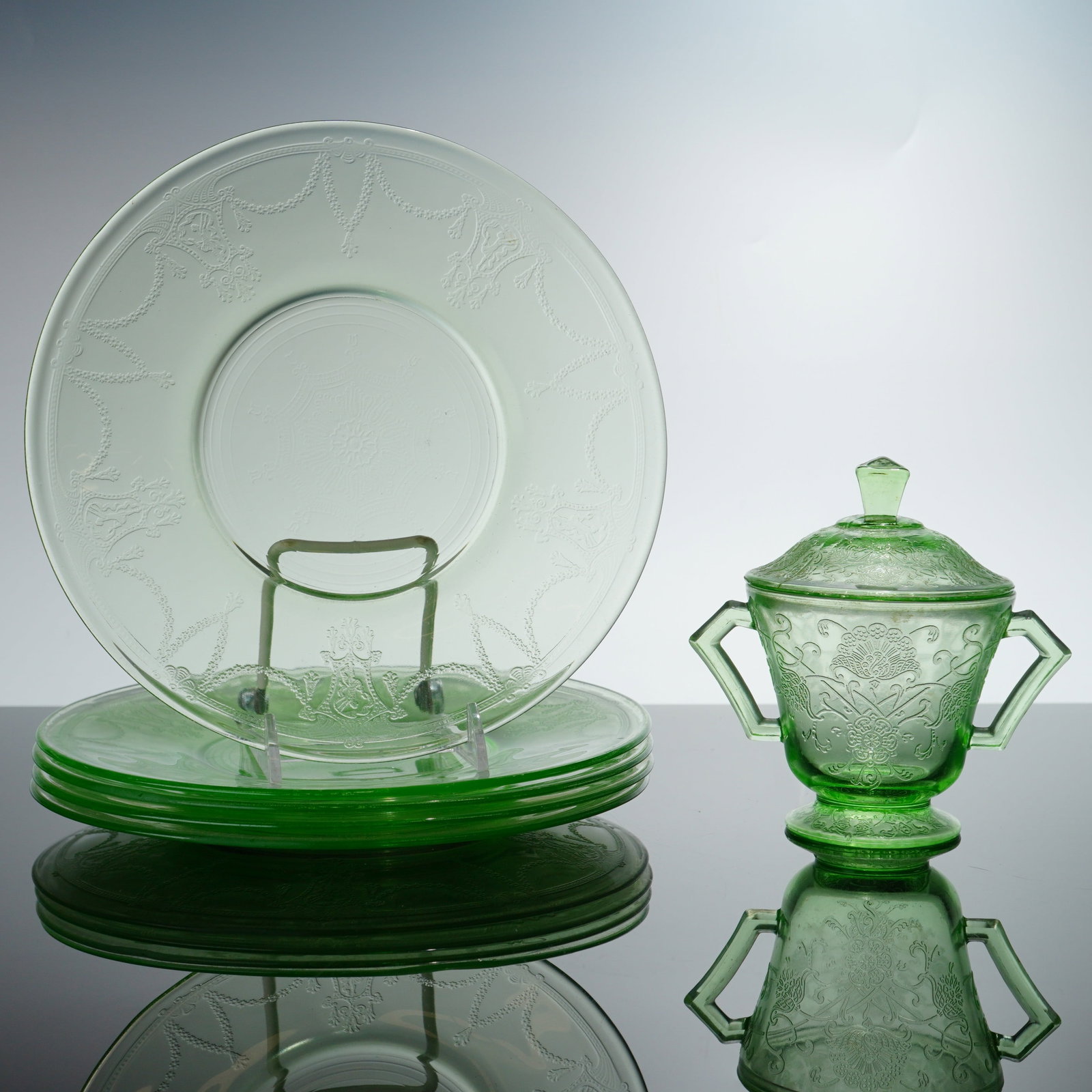 Collection of Six Green Depression Glass in Cameo and Florentine No. 1 Patterns: This collection of depression green glass consists of multiple plates and a covered sugar bowl. The plates are in the Cameo pattern, also referred to as Ballerina or Dancing Girl, and are attributed t