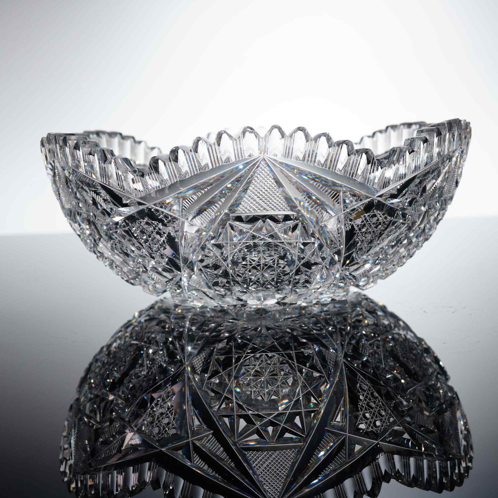 Johnson Cut Crystal Bowl with Sawtooth Edge: This Johnson cut crystal bowl is crafted from heavy leaded crystal in the American Brilliant Period style. The body features an intricate, deeply cut geometric design consisting of multiple hobstars, 