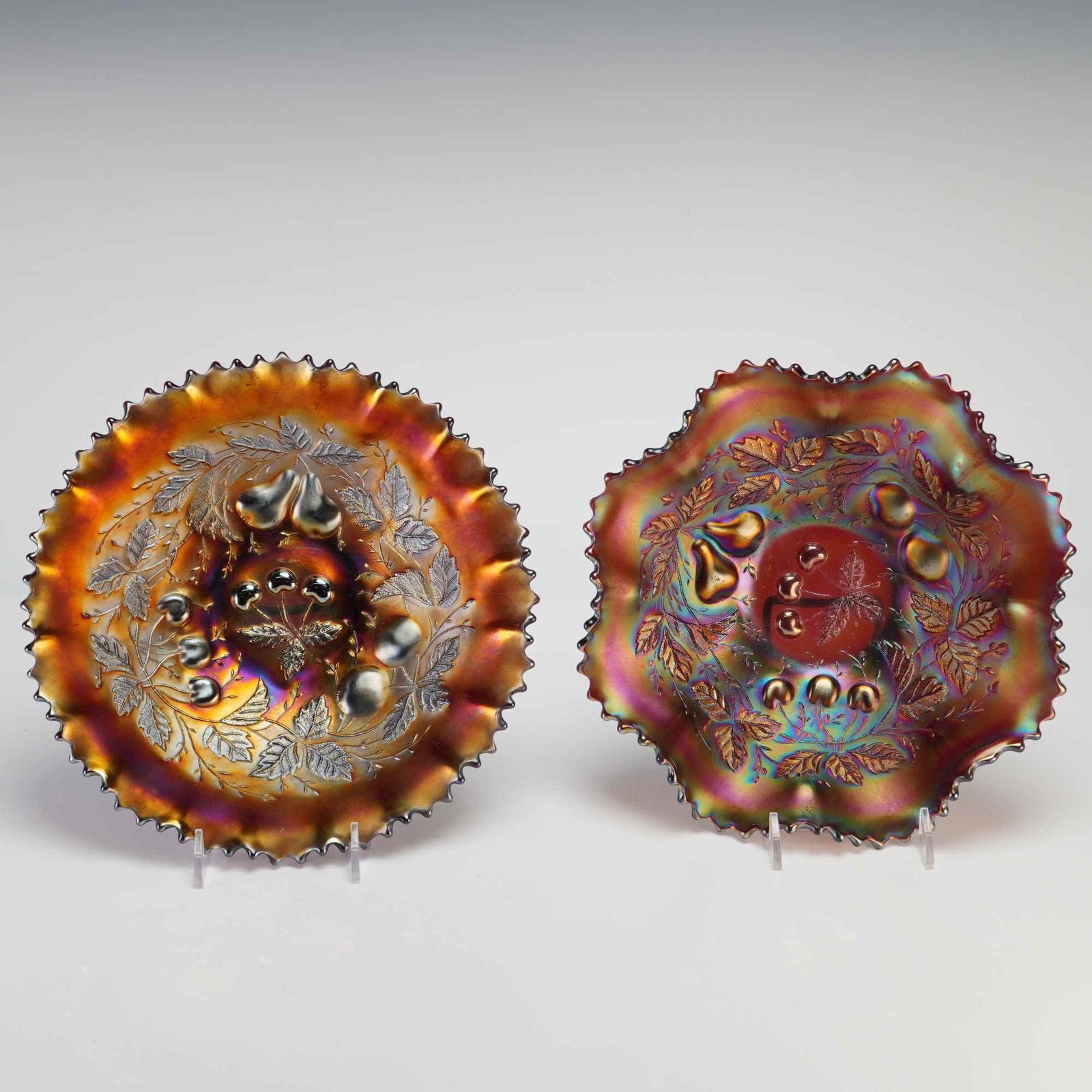 A Pair of Northwood Amethyst Three Fruits Carnival Glass Bowls: This pair of pressed carnival glass bowls features the Three Fruits interior pattern and a Basket Weave exterior pattern. The Three Fruits motif consists of embossed pears, cherries, and foliage radia
