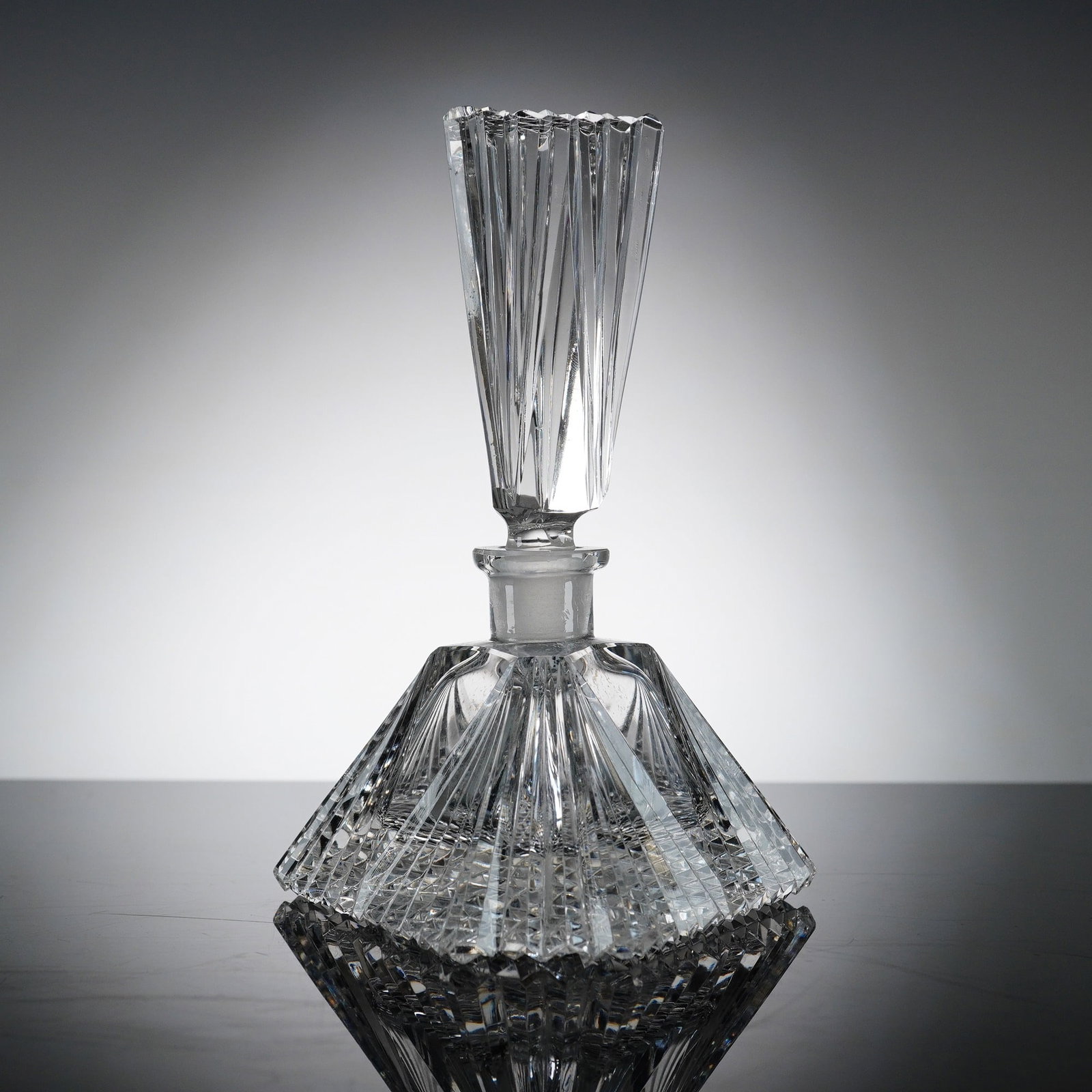 Art Deco Style Pyramid Cut Crystal Perfume Bottle with Stopper: This heavy lead crystal perfume bottle features a bold, geometric form in the shape of a triangular pyramid. The bottle is decorated with a complex array of hand-cut patterns, including a dense diamon