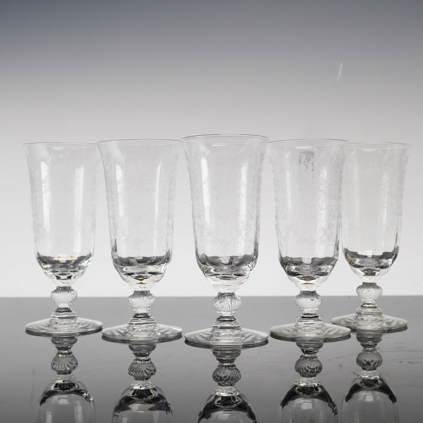 5pc Heisey Orchid Etched Crystal Flutes: This set of stemmed crystal glasses is produced by Heisey in the Orchid pattern. The glasses feature a flared, tulip-shaped bowl decorated with wheel-etched floral motifs including a central orchid bl