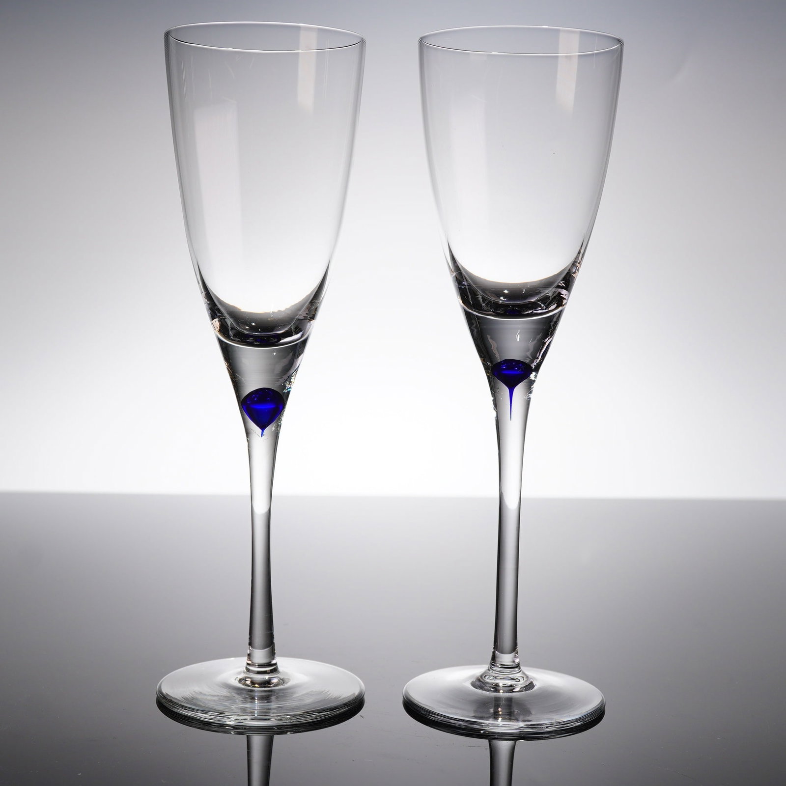 A Pair Crystal Wine Glasses: A pair of stemmed crystal glasses, atributed to Orrefors. Each glass features a tall, tapering bowl suitable for wine, supported by a slender stem and a circular foot. The defi?ning characteristic is 