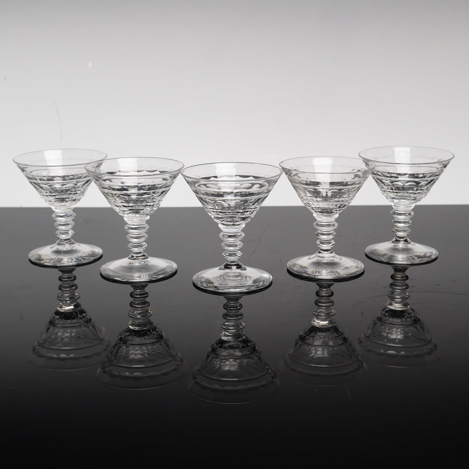 Set of Five Cut Crystal Cocktail Glasses with Annulated Stems: A set of five lead crystal cocktail or coupe glasses featuring a design attributed to Stuart England in the Oleta pattern. Each glass is composed of a conical bowl with a flared rim, decorated with ho