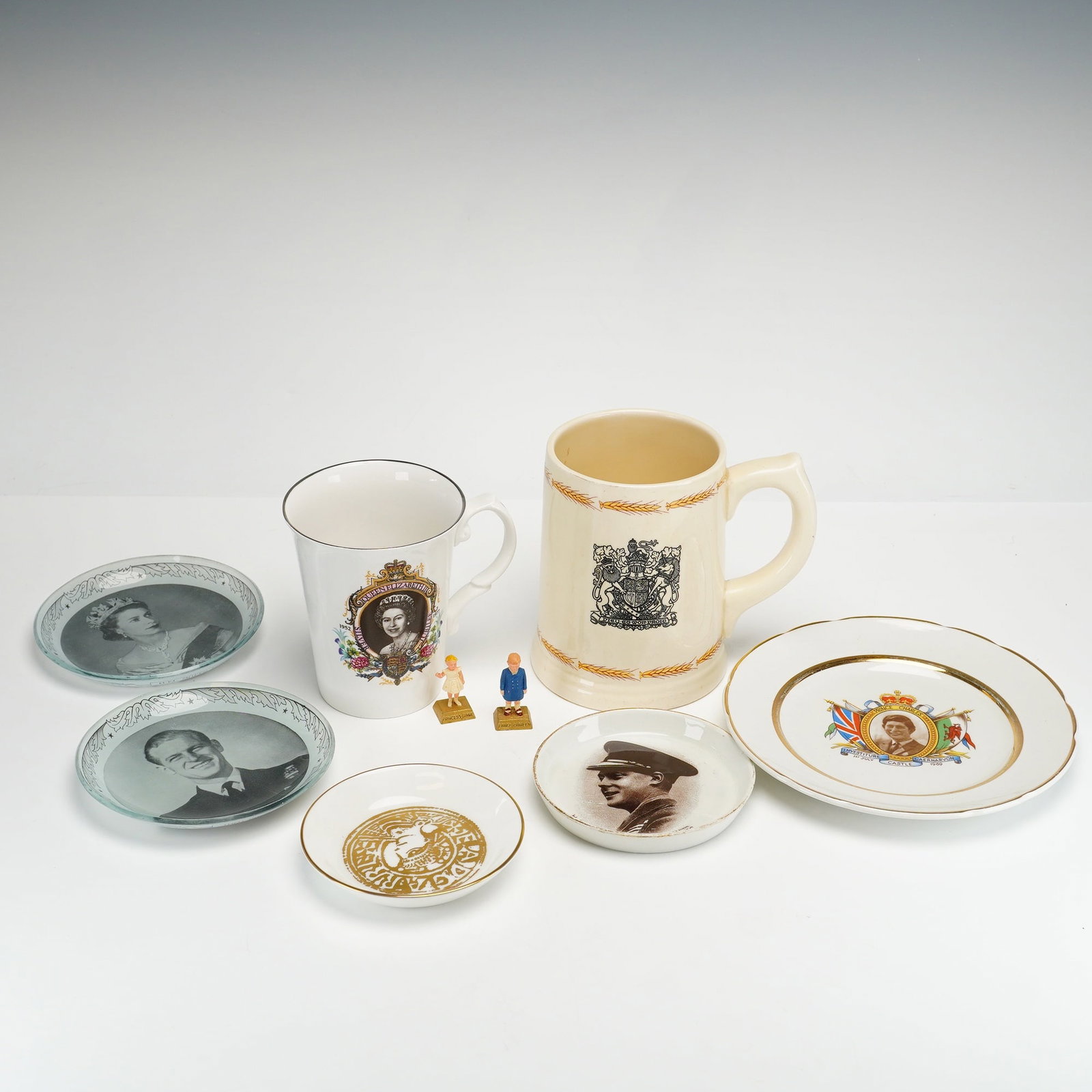 9pc Collection of British Royal Family Commemorative Ceramics and Glassware: This collection of British royalty commemorative items includes ceramics, glass, and figures, documenting the ER reign and misc English royalty. The assortment features a large cream-colored stoneware