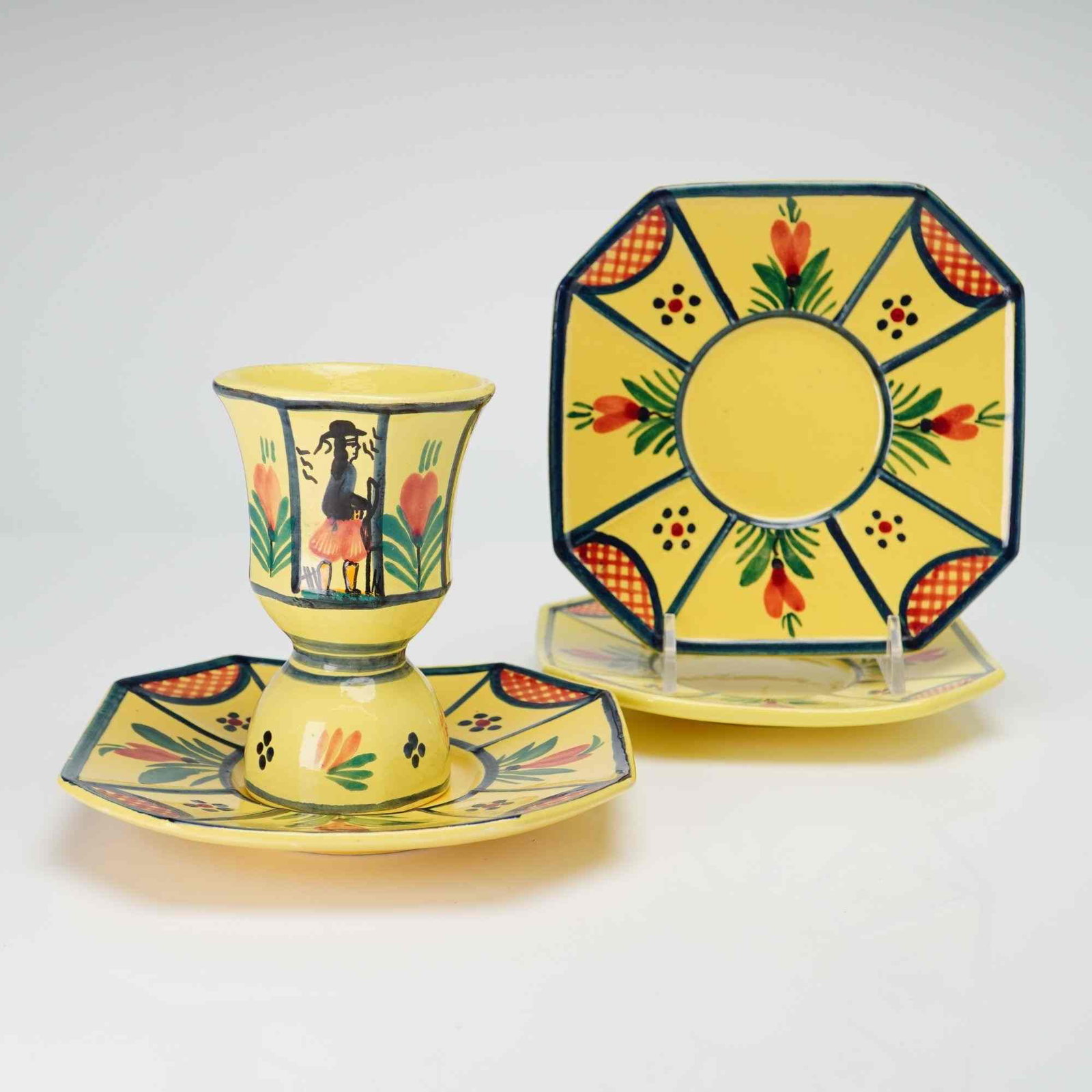 4pc HB Quimper Soleil Yellow Faience Double Egg Cup and Three Octagonal Saucers: The earthenware items feature hand-painted decoration over a bright yellow ground. The double-ended egg cup is designed with a waisted center and features a central panel depicting a Petit Breton figu