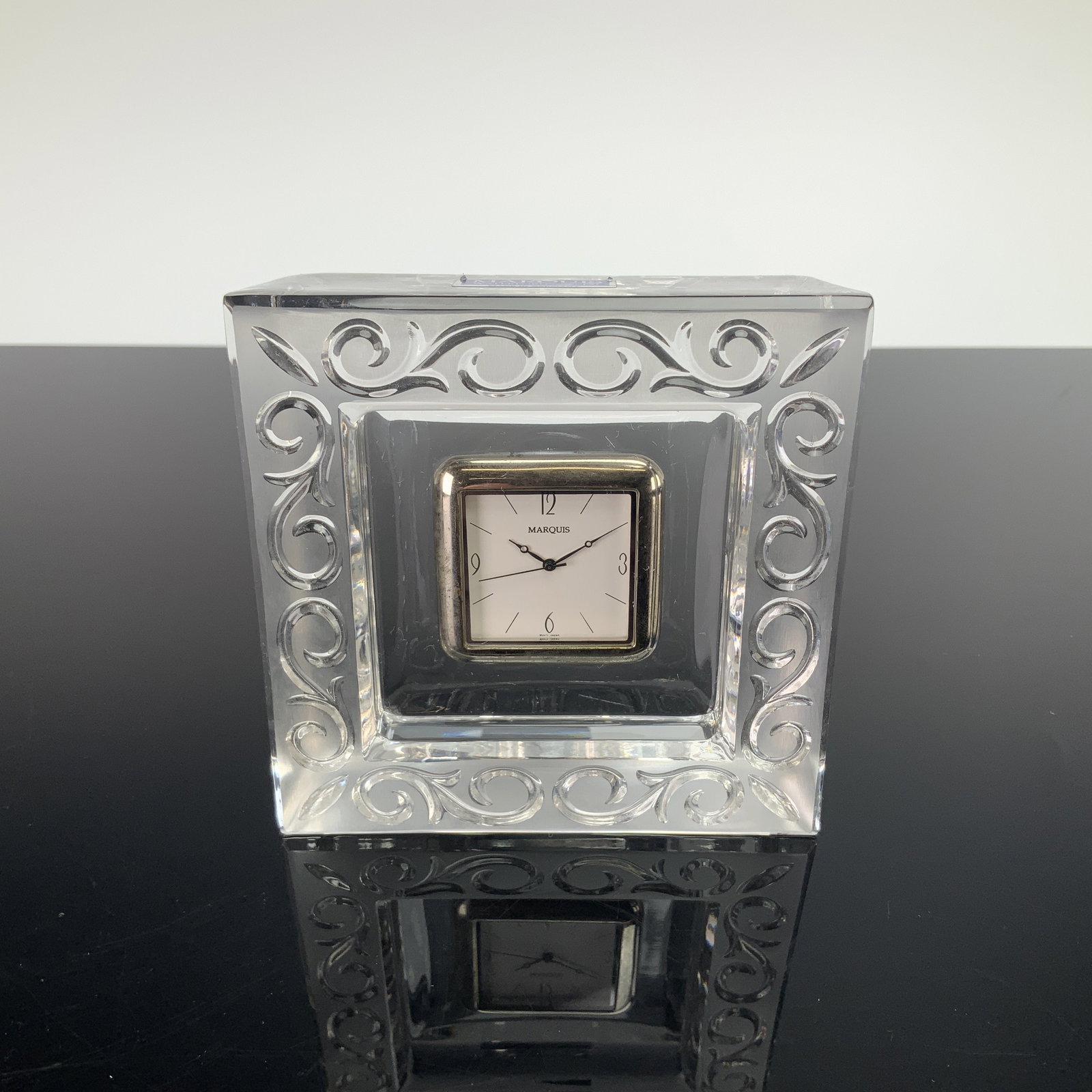 Marquis by Waterford Arabesque Crystal Square Desk Clock: A Marquis by Waterford Arabesque pattern square crystal table or desk clock. The case is constructed from clear lead crystal featuring a molded and cut scrollwork border. The central square clock modu