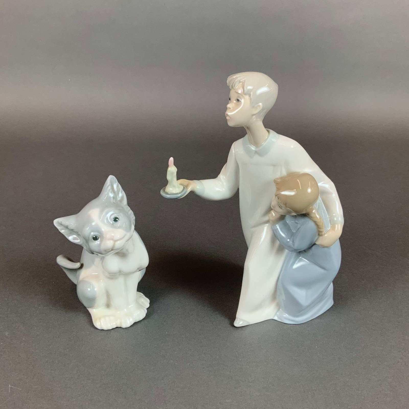Two Lladro Glazed Porcelain Figurines, Boy and Girl and Cat: This lot features two glazed porcelain figurines produced by Lladro in Spain. The first figurine, titled Boy & Girl (Model 4874), depicts a boy in a white and pale blue gown holding a small chambersti