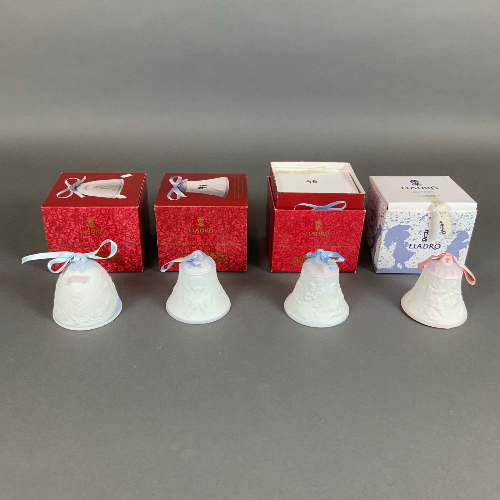 Set of Four Lladro Matte Porcelain Annual Christmas Bells with Boxes: A set of four Lladro annual Christmas bells crafted from matte bisque porcelain with relief-molded decoration. Each bell features a distinct thematic bas-relief design: one featuring floral and angeli