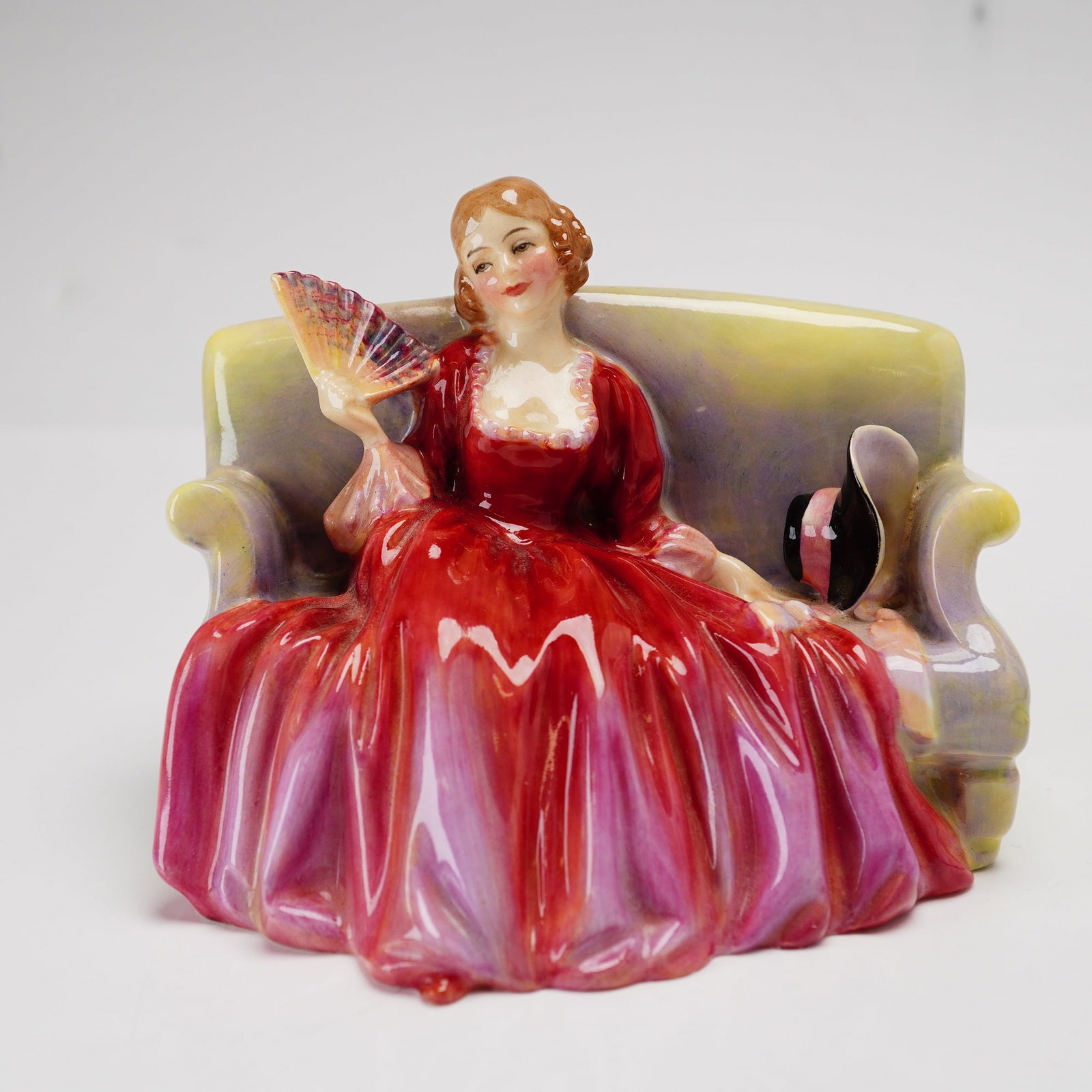 Royal Doulton Figurine Sweet and Twenty HN1610: This Royal Doulton glazed porcelain figurine, titled Sweet and Twenty, is model number HN 1610. The piece depicts a woman in a period costume style, featuring a voluminous red and pink gown, seated on