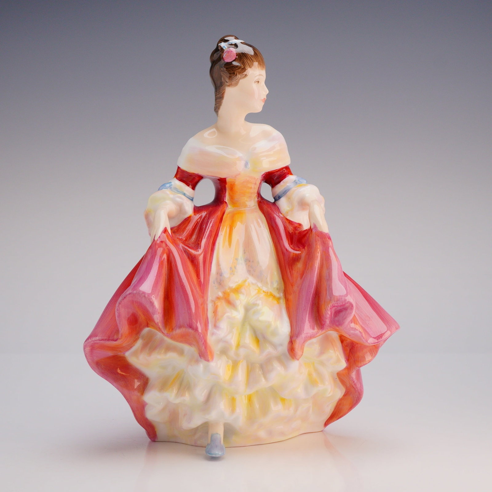 Royal Doulton Figurine, Southern Belle HN2229: The figure depicts a standing woman in a voluminous period gown, richly glazed and hand-painted primarily in deep shades of red, pink, and yellow, with light blue accents on the sleeves. The base feat