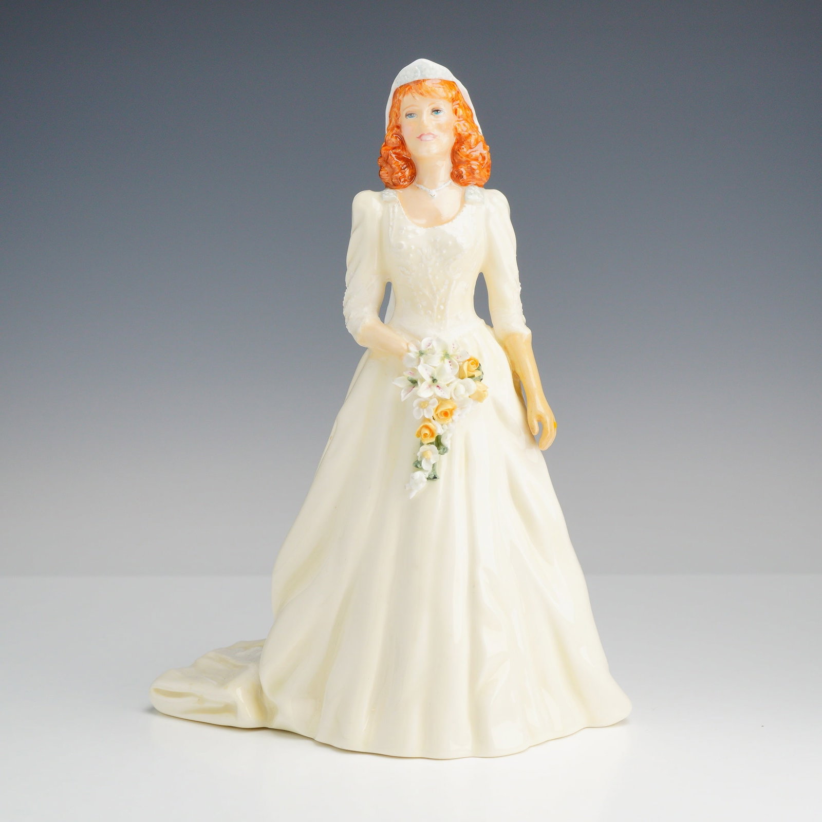 Royal Doulton Limited Edition Bone China Figurine, The Duchess of York HN3086: This glazed bone china figure depicts Sarah Ferguson in her 1986 wedding gown, featuring her characteristic red hair, a cream-colored dress with a long train, and a flowing white veil. She is shown ca