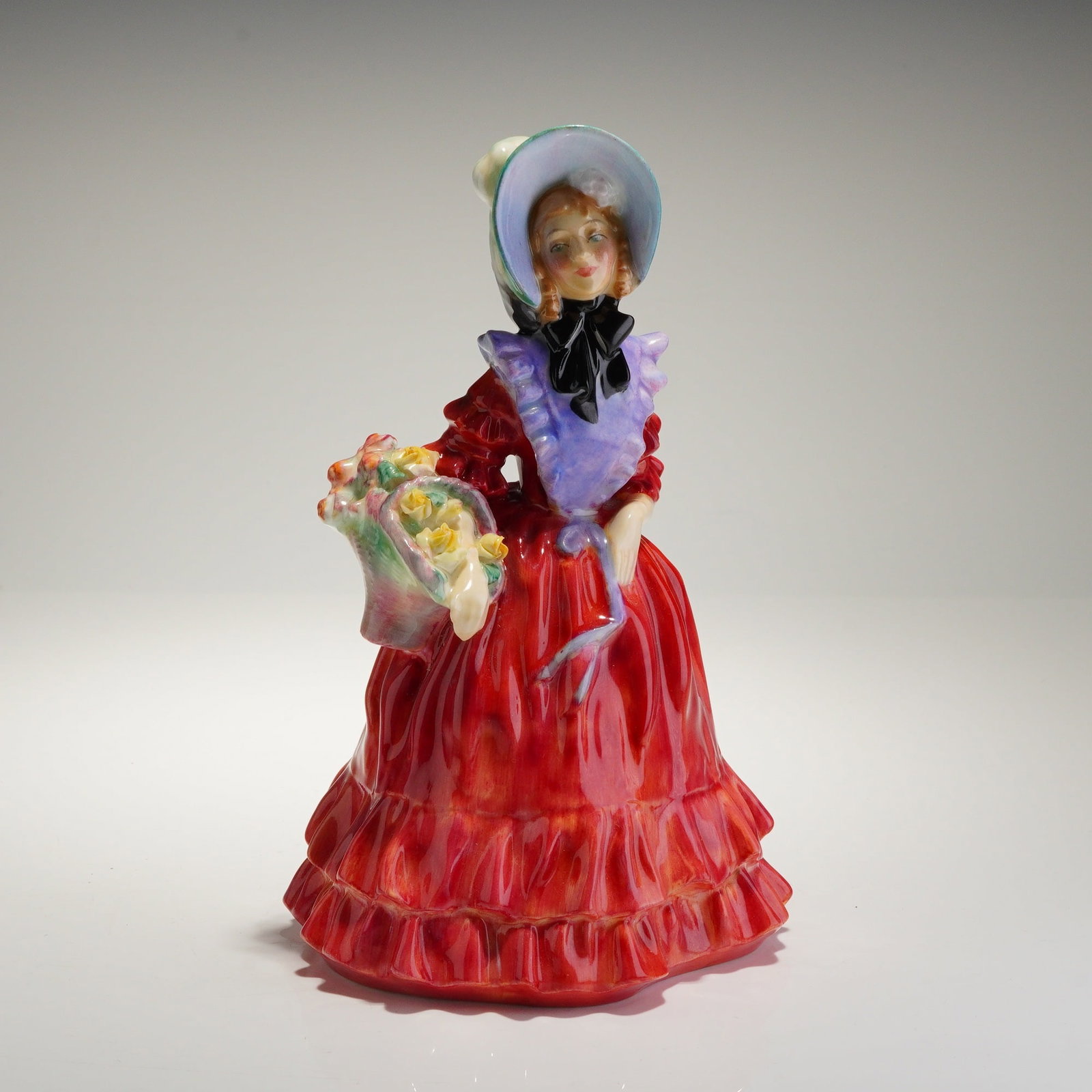 Royal Doulton Porcelain Figurine Lady Betty HN1967: A single Royal Doulton bone china figurine, model 'Lady Betty' (HN1967), depicting a woman wearing a voluminous, ruffled gown glazed in bright red, accented by a lavender collar piece and a black bow 