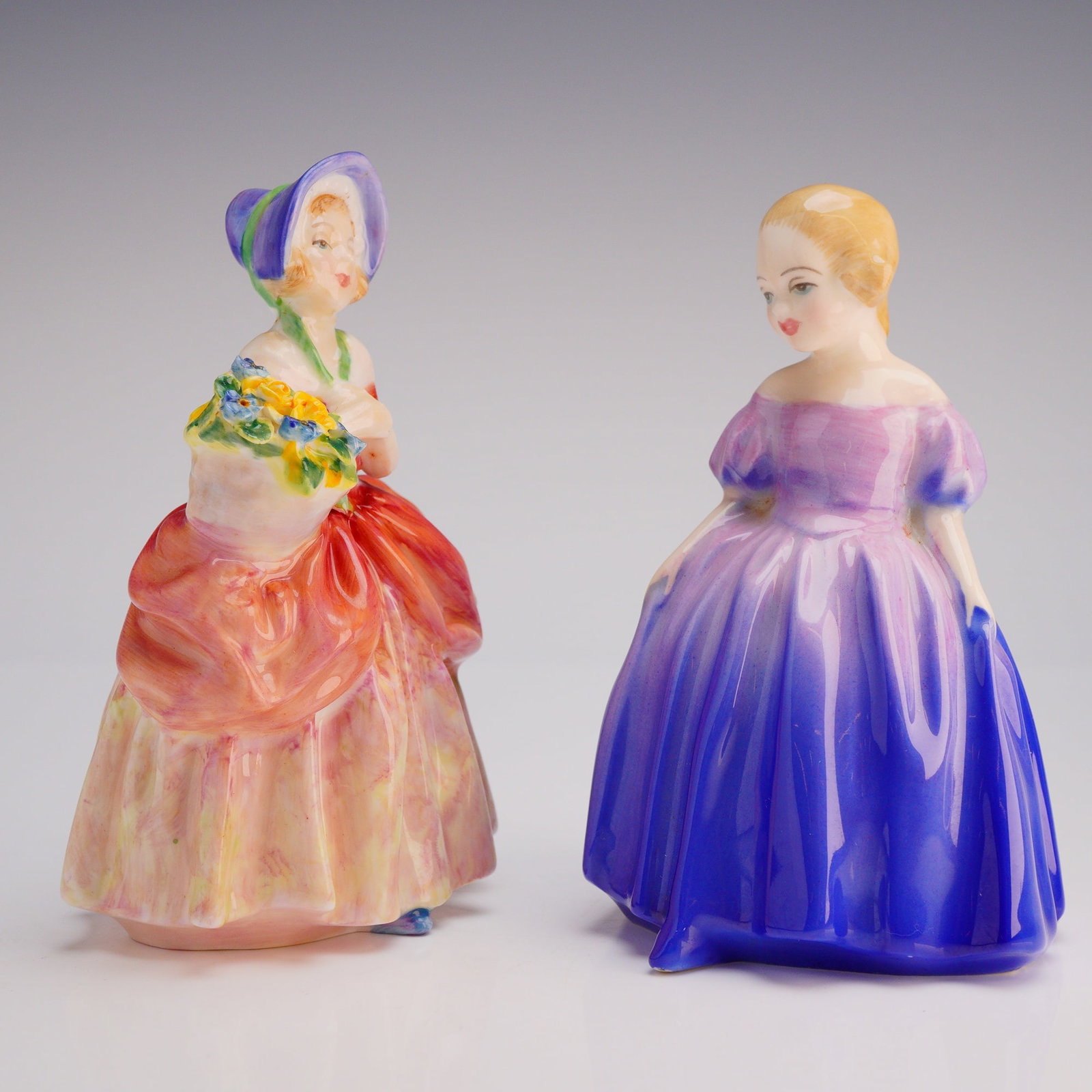 2pc Royal Doulton Figurines Marie HN1370 and Cissie HN1809: Both figures depict young women in stylized 18th or 19th-century attire, executed in hand-painted coloration and finished with a high gloss glaze. Cissie (HN 1809, COPR. 1937) is dressed in an orange 