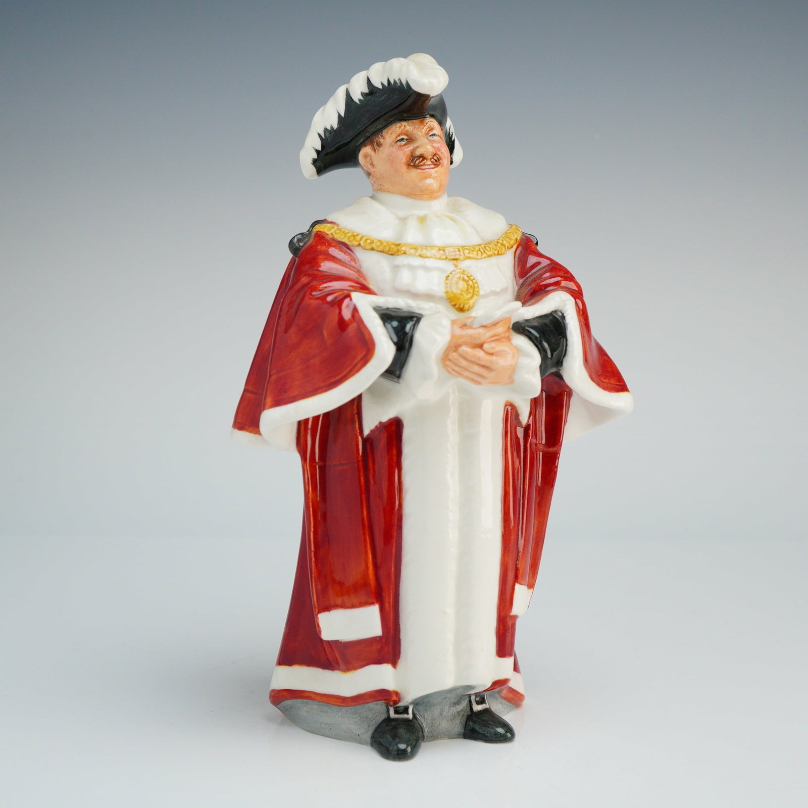 Royal Doulton Figurine The Mayor HN2280: This mid-20th-century figure is depicted in traditional ceremonial regalia, including a long red robe with white trim, a white jabot, and a gold-toned chain of office featuring a central medallion. Th