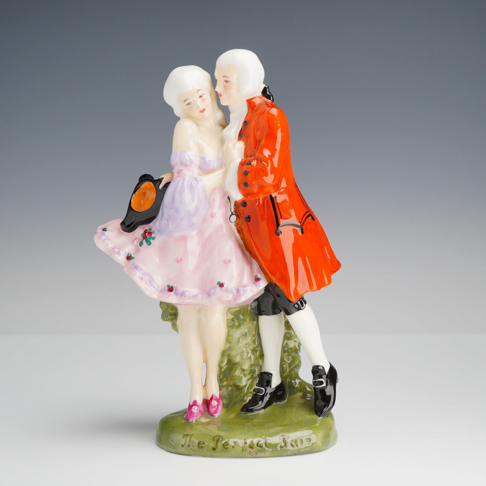 Royal Doulton Porcelain Figurine, The Perfect Pair HN581: The piece features a man and woman in mid-18th-century costume, with the male figure in a vibrant orange-red frock coat and the female figure in a pink and lavender gown holding a tricorn hat. The fig