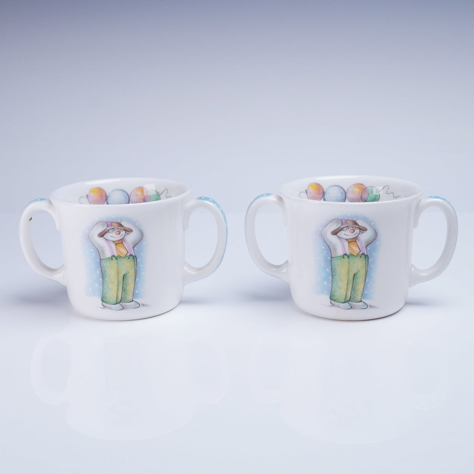 2pc Royal Doulton The Snowman Gift Collection Double-Handled Mugs: A group of Royal Doulton two-handled mugs constructed of white bone china, manufactured in England as part of "The Snowman Gift Collection." The mugs date to 1988. Each mug features transfer-printed i