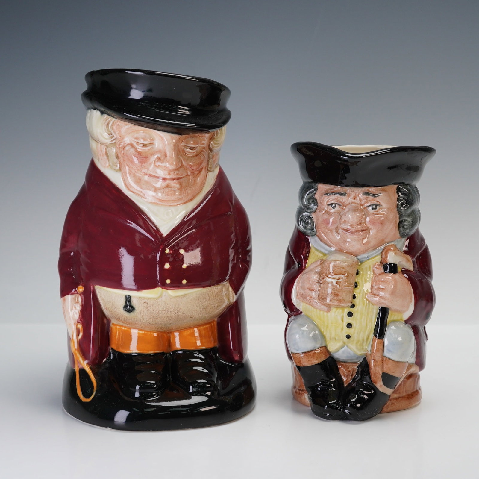 2pc Royal Doulton Large Toby Jugs, The Huntsman and Jolly Toby: The Huntsman features a portly figure dressed in a deep red coat and black hat, holding a whip in one hand and exuding a look of quiet authority. Jolly Toby is shown seated with a cheerful expression,