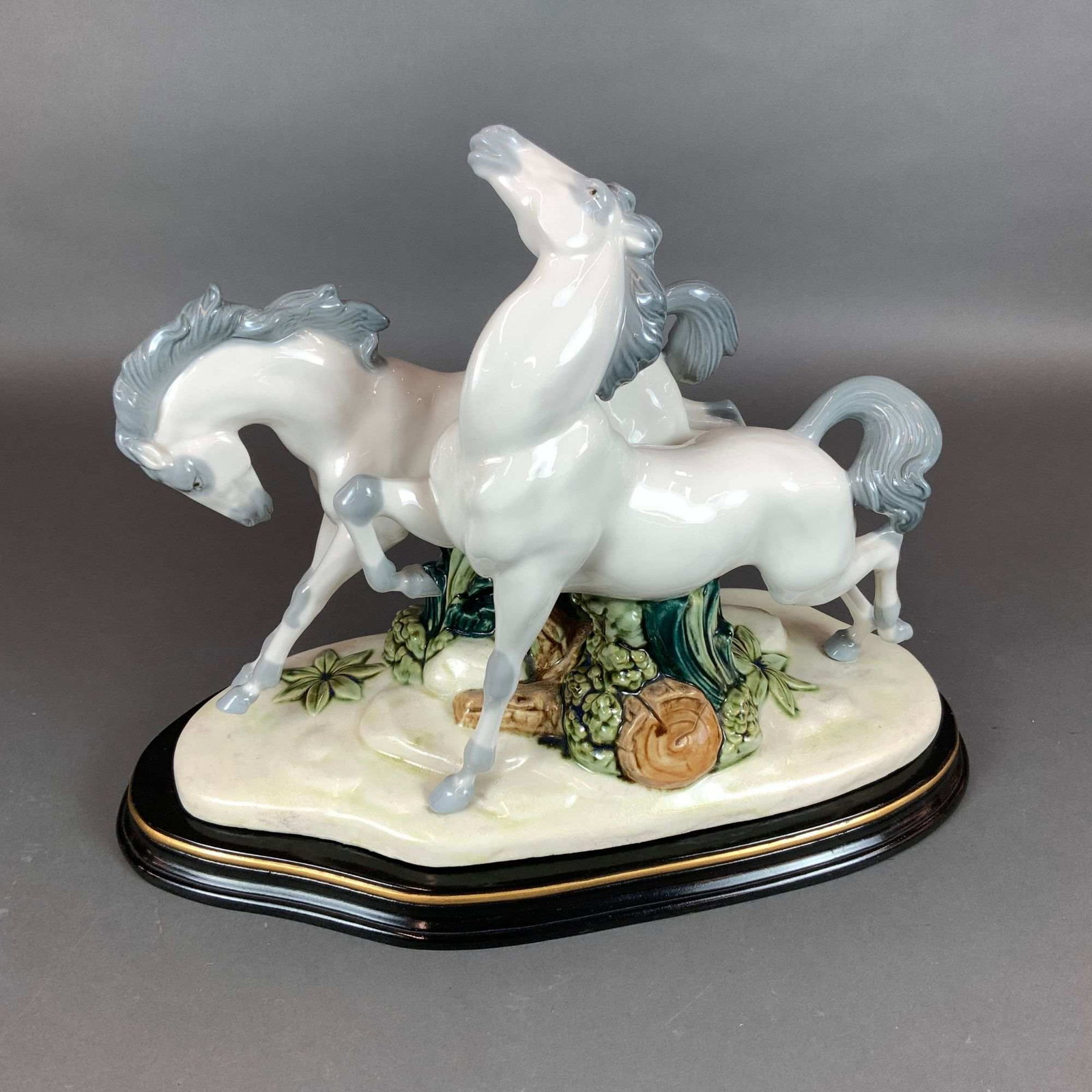 Nadal Ceramic Figurine of Two Galloping Horses with Wooden Base: A large Spanish porcelain figurine by Nadal depicting two horses in a dynamic, overlapping galloping pose. The sculpture is finished in a high-gloss glaze with the horses rendered in a pale off-white 