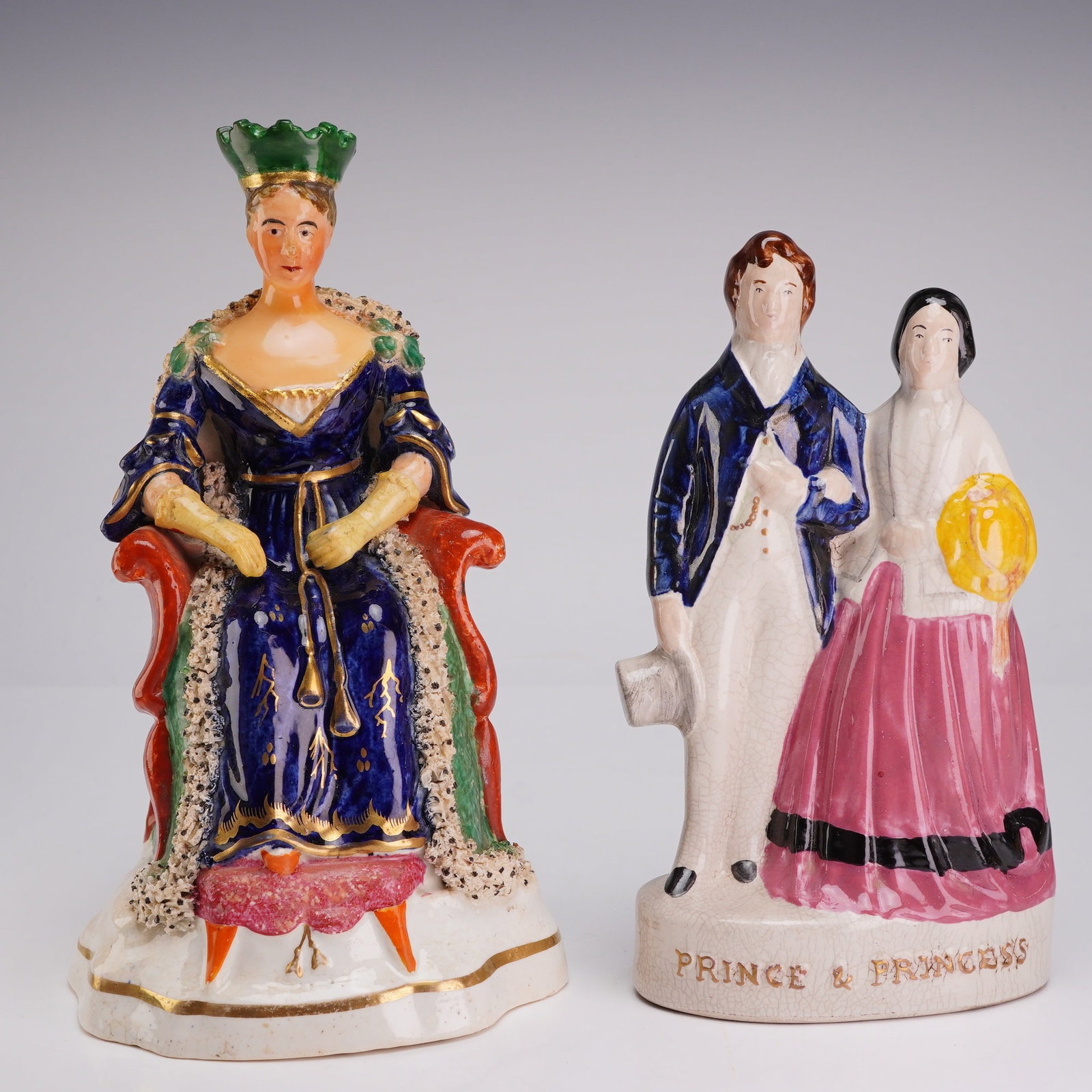 2pc 19th Century Staffordshire Earthenware Royal Figures of Queen Victoria & Prince of Wales: Two 19th-century Staffordshire lead-glazed earthenware figurines depicting British royalty. The first figure represents Queen Victoria seated on a high-backed red throne. She is modeled wearing a gree