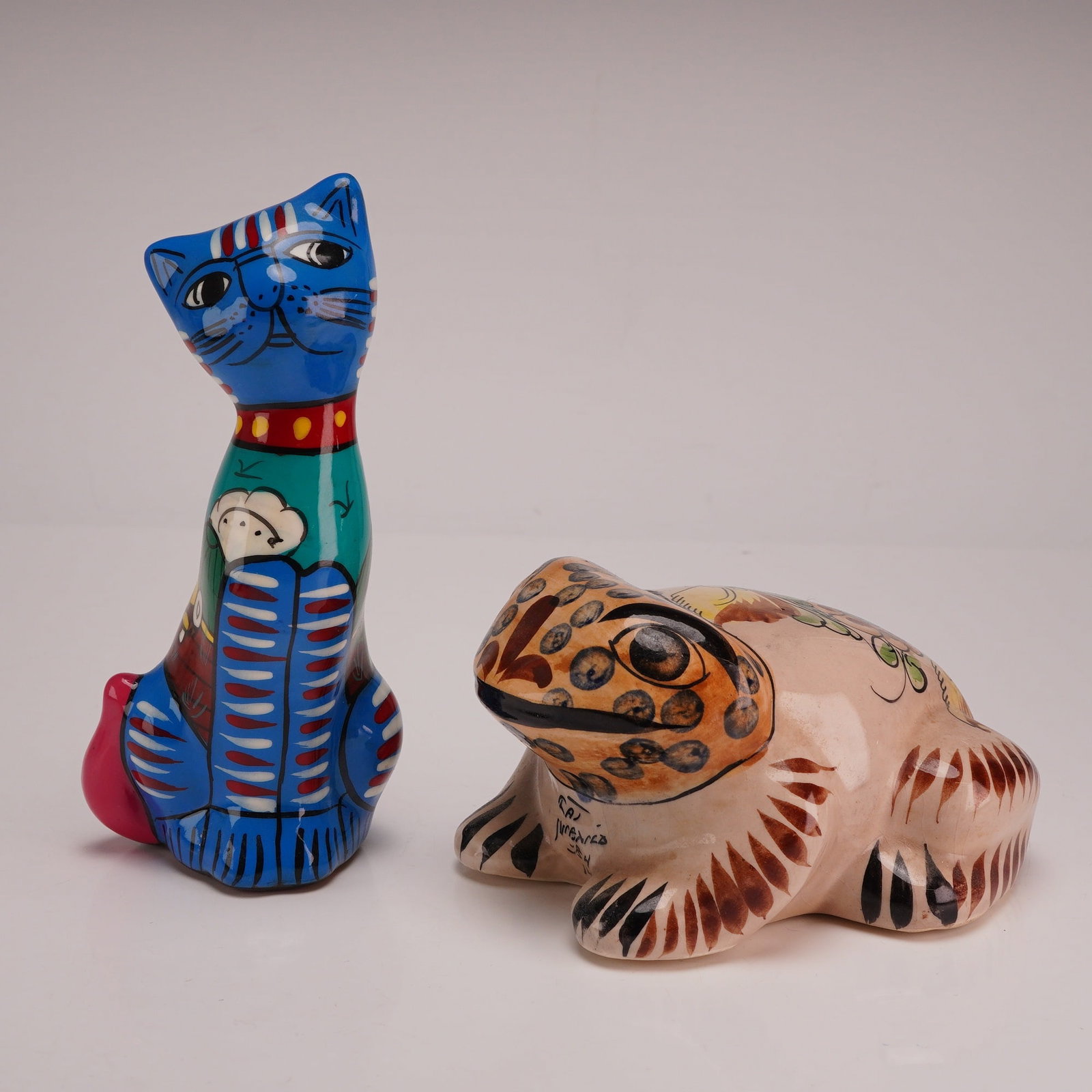 2pc Mexican Talavera Hand Painted Ceramic Cat & Frog Figurines: This set of two Mexican Talavera folk art ceramic hand-painted animal figures includes one frog and one cat. The cat figurine is a tall, slender stylized figure featuring a blue head and neck, a red c