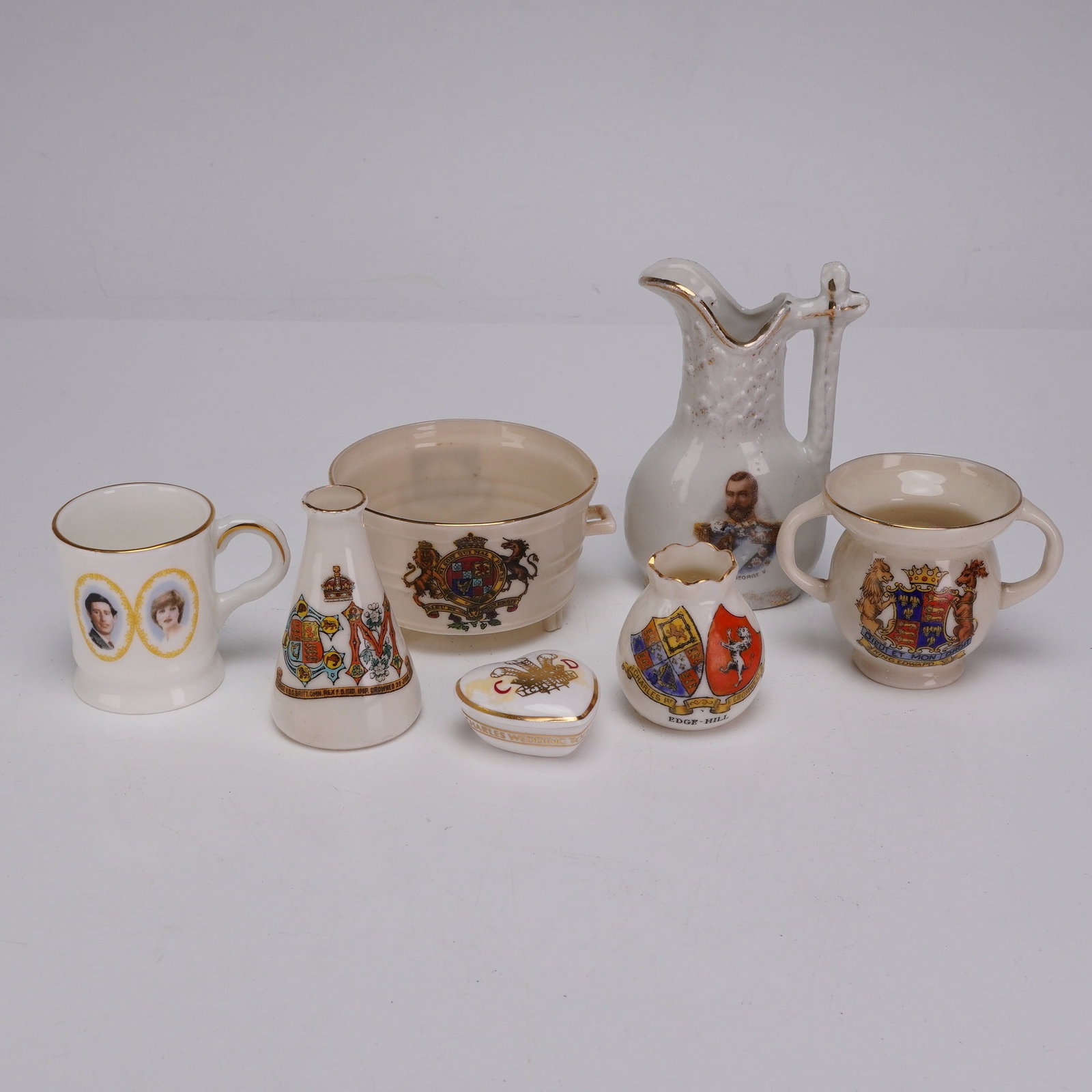Collection of Seven English Crested Ware and Royal Commemorative Ceramic Miniatures: A collection of seven English ceramic commemorative miniatures and crested ware pieces manufactured by various Staffordshire potteries. The lot includes a Coalport fine bone china mug commemorating th
