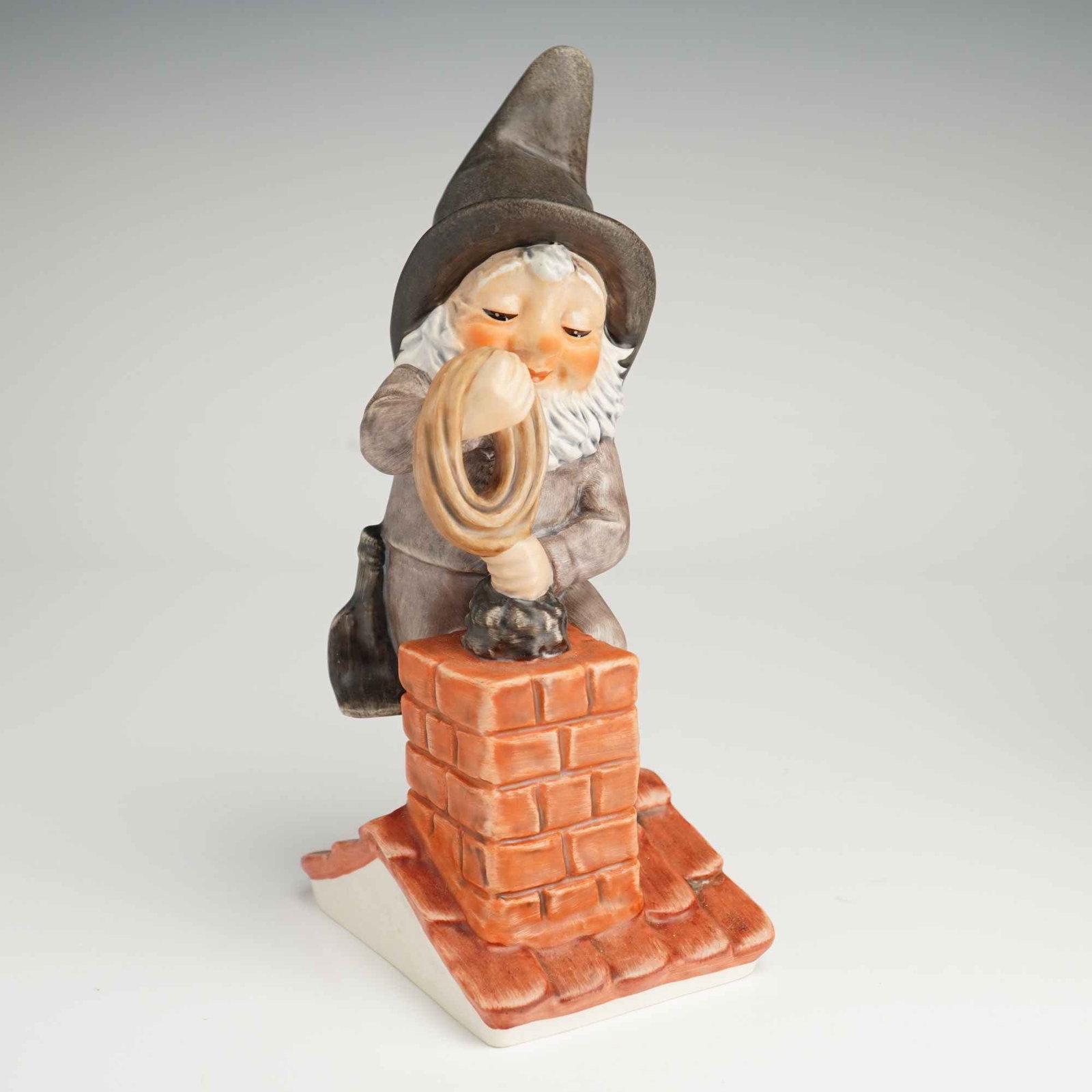 Goebel Co-Boy Chuck the Chimney Sweep Figurine: This Goebel porcelain figurine from the Co-Boy collection depicts the character Chuck the Chimney Sweep. The figure is rendered in a multi-toned matte and glazed finish, featuring a white beard, a tal