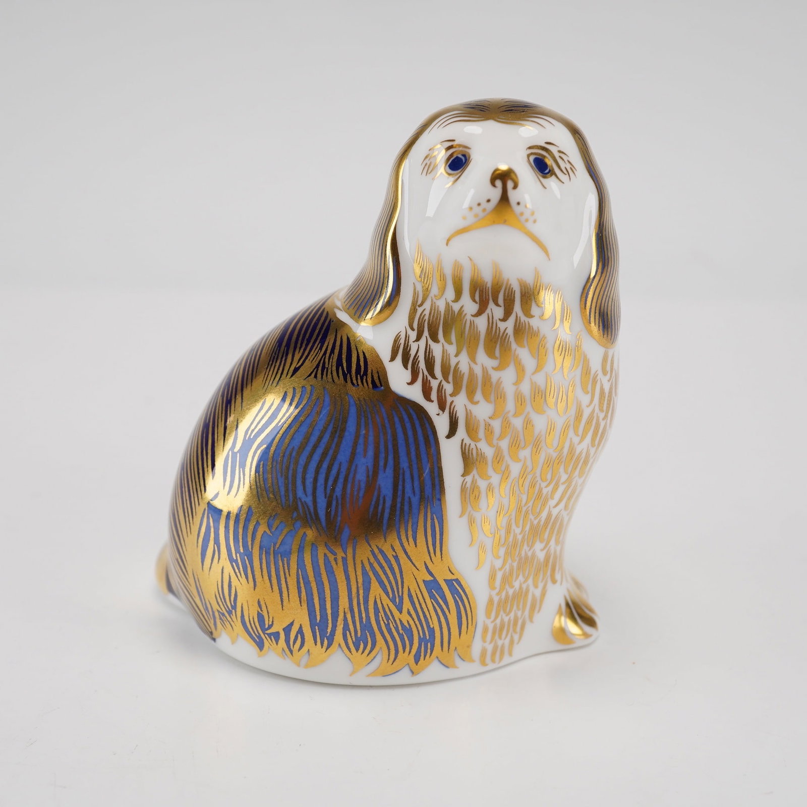 Royal Crown Derby Bone China Paperweight, King Charles Spaniel: This piece is crafted from fine English bone china and features an Imari-inspired decorative scheme. The design utilizes a white ground accented with deep cobalt blue and extensive 22 karat gold gildi