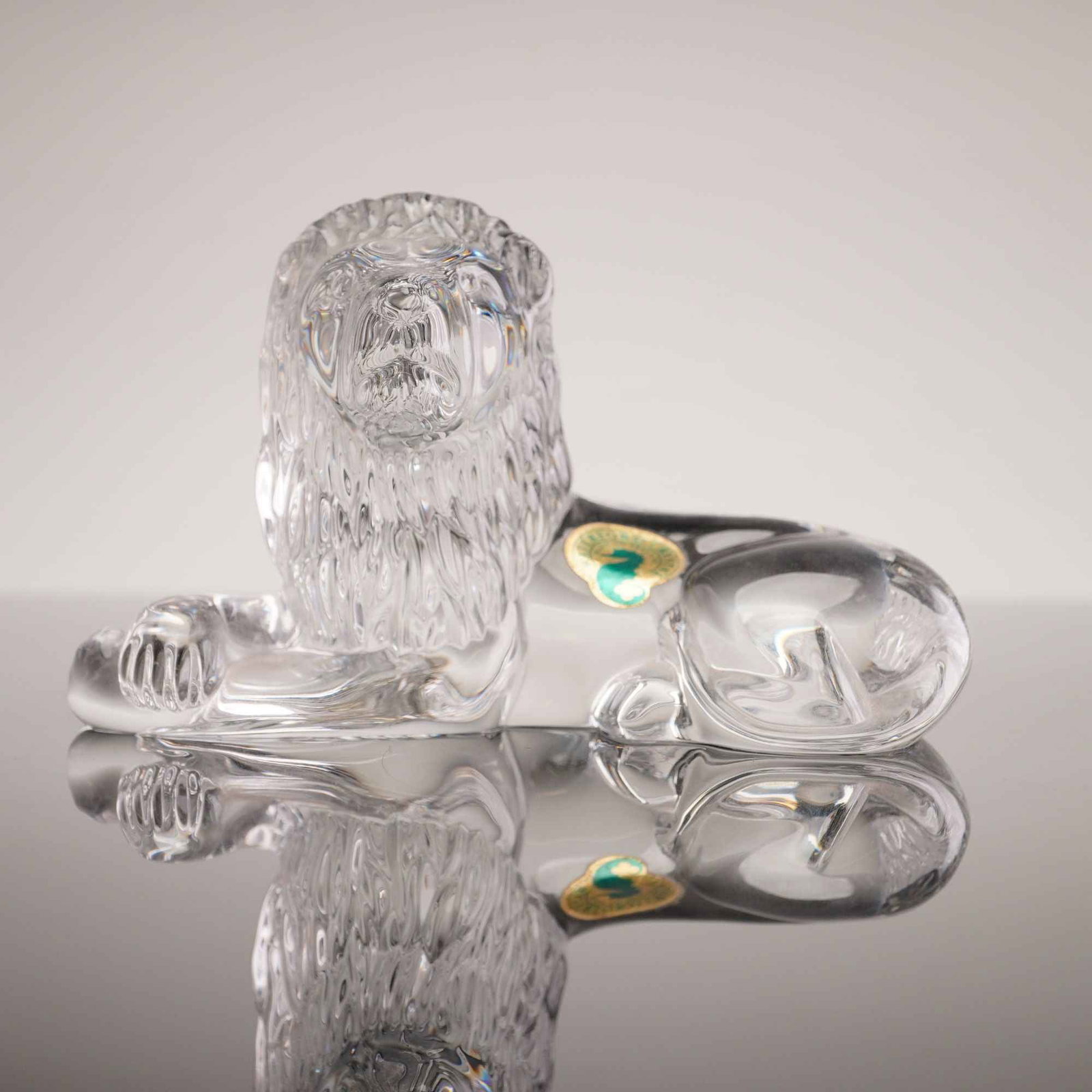 Waterford Crystal Reclining Lion Figurine: A solid lead crystal figurine depicting a reclining male lion with its head turned forward. The figure features a detailed, textured mane and a smooth, polished body. An acid-etched Waterford maker ma