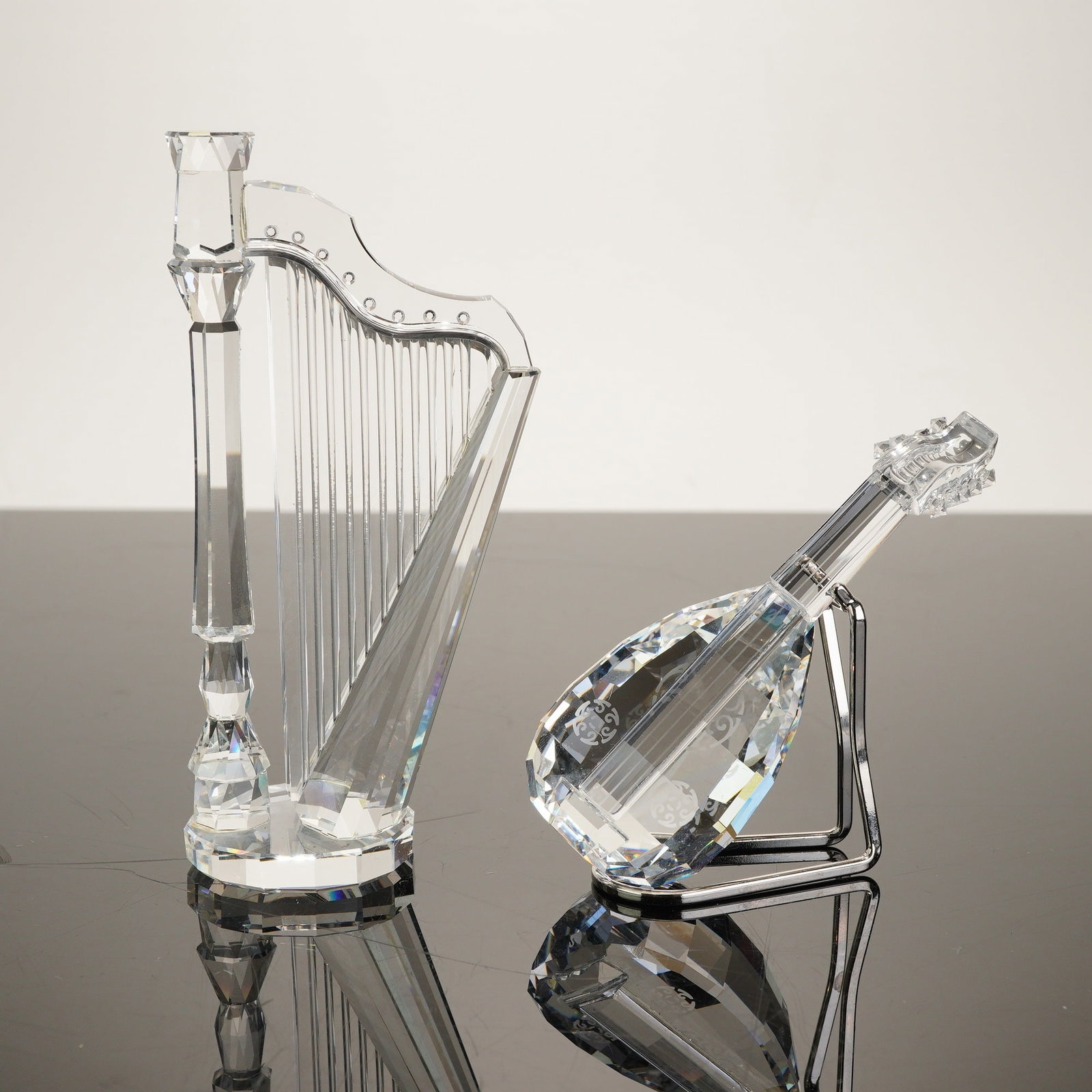 Swarovski Crystal Melodies Series 2pc Crystal Figurines Guitar and Harp, 1992: Maker: Swarovski. Model: Crystal Melodies Series Harp (7477 000 003) and Lute/Guitar (7477 000 001). Serial: Acid-etched Swarovski swan logo. Materials: Multi-faceted clear Austrian lead crystal and s