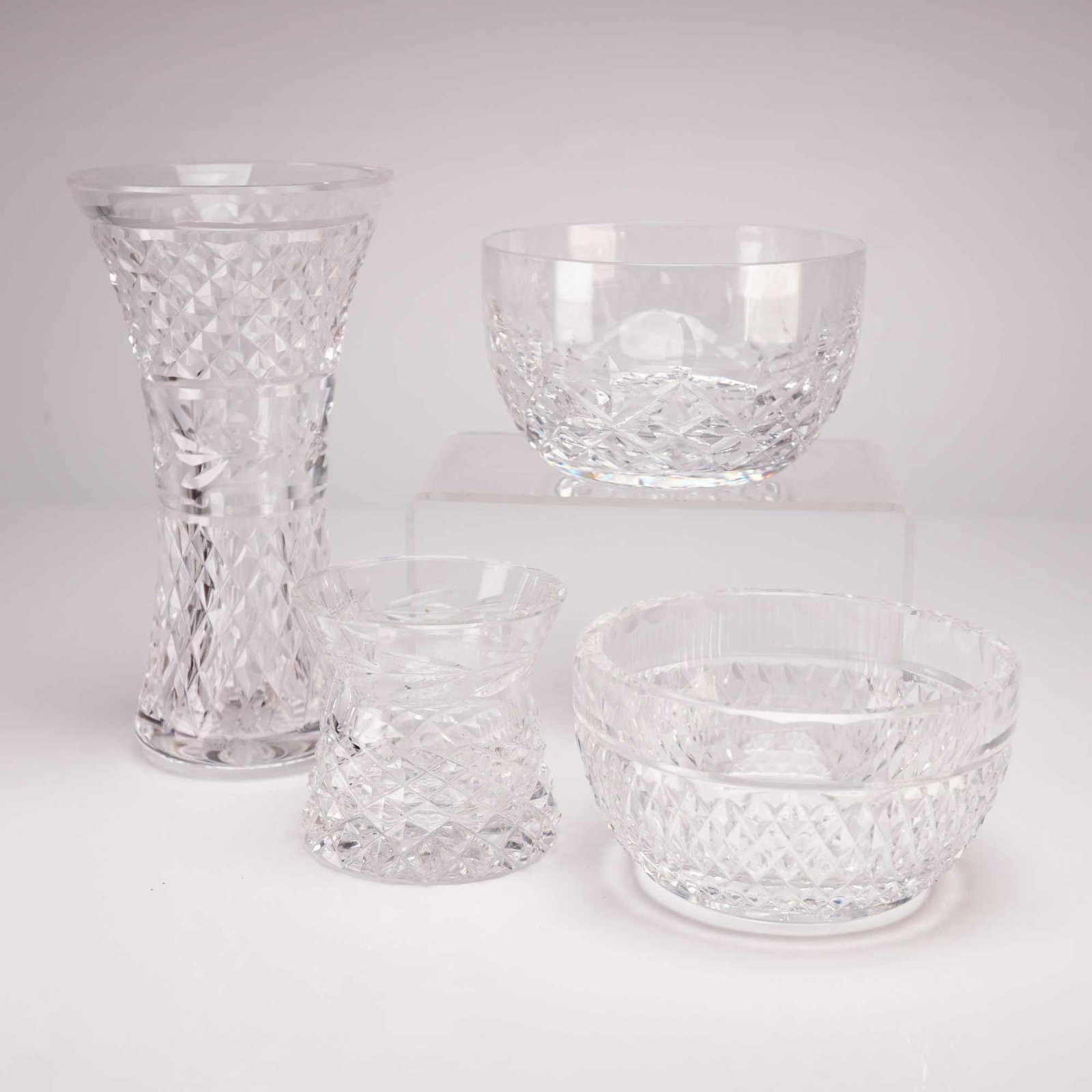 Waterford Crystal Glandore Pattern Four-Piece Grouping: This four-piece grouping of fine cut lead crystal is manufactured by Waterford in the classic Glandore pattern. The collection includes one tall flared vase with an elegant hourglass silhouette and ci