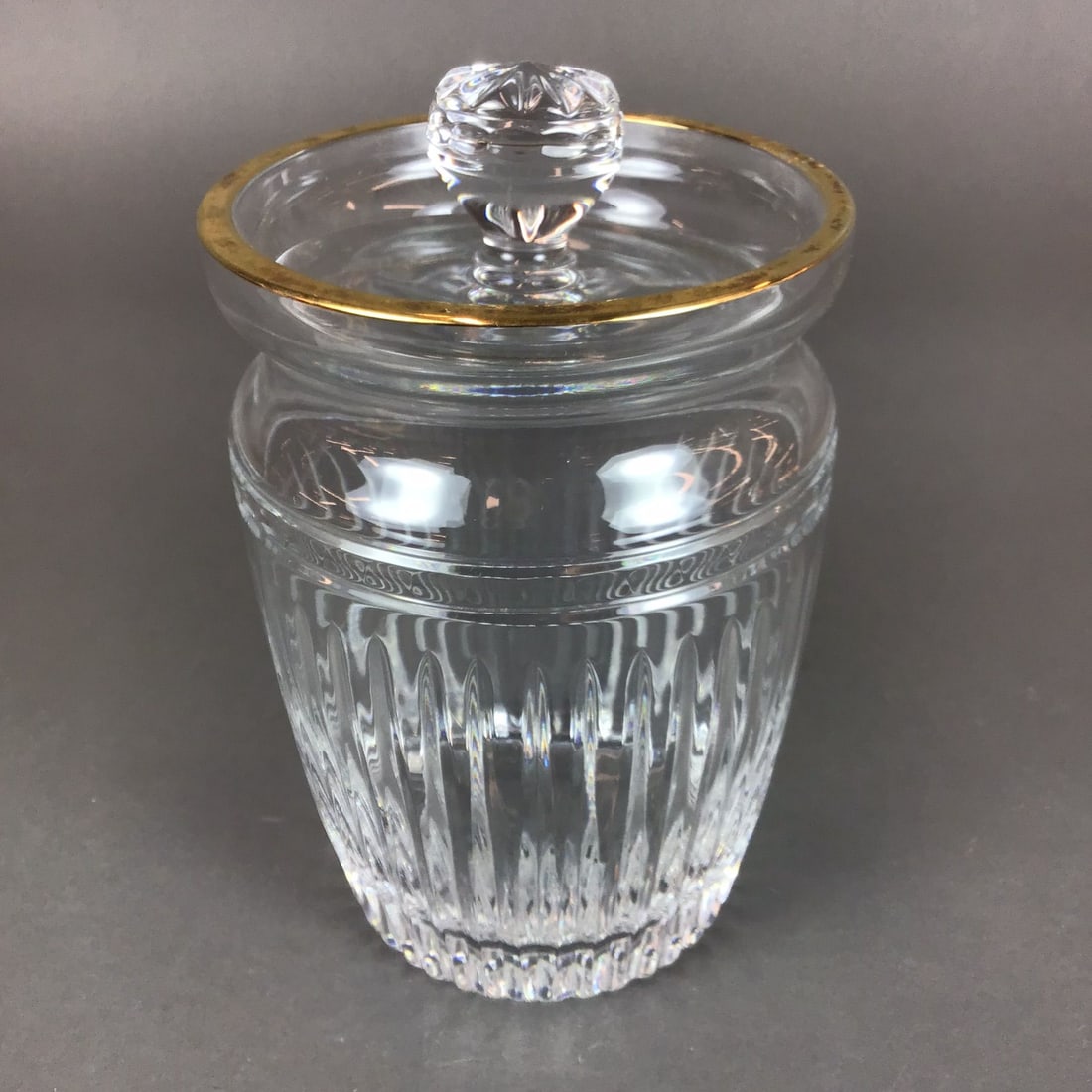Marquis by Waterford Canterbury Crystal Biscuit Jar with Lid: This crystal biscuit jar is produced by Marquis by Waterford in the Canterbury pattern. The vessel features a tapered barrel form decorated with vertical flute cuts around the body and a decorative et