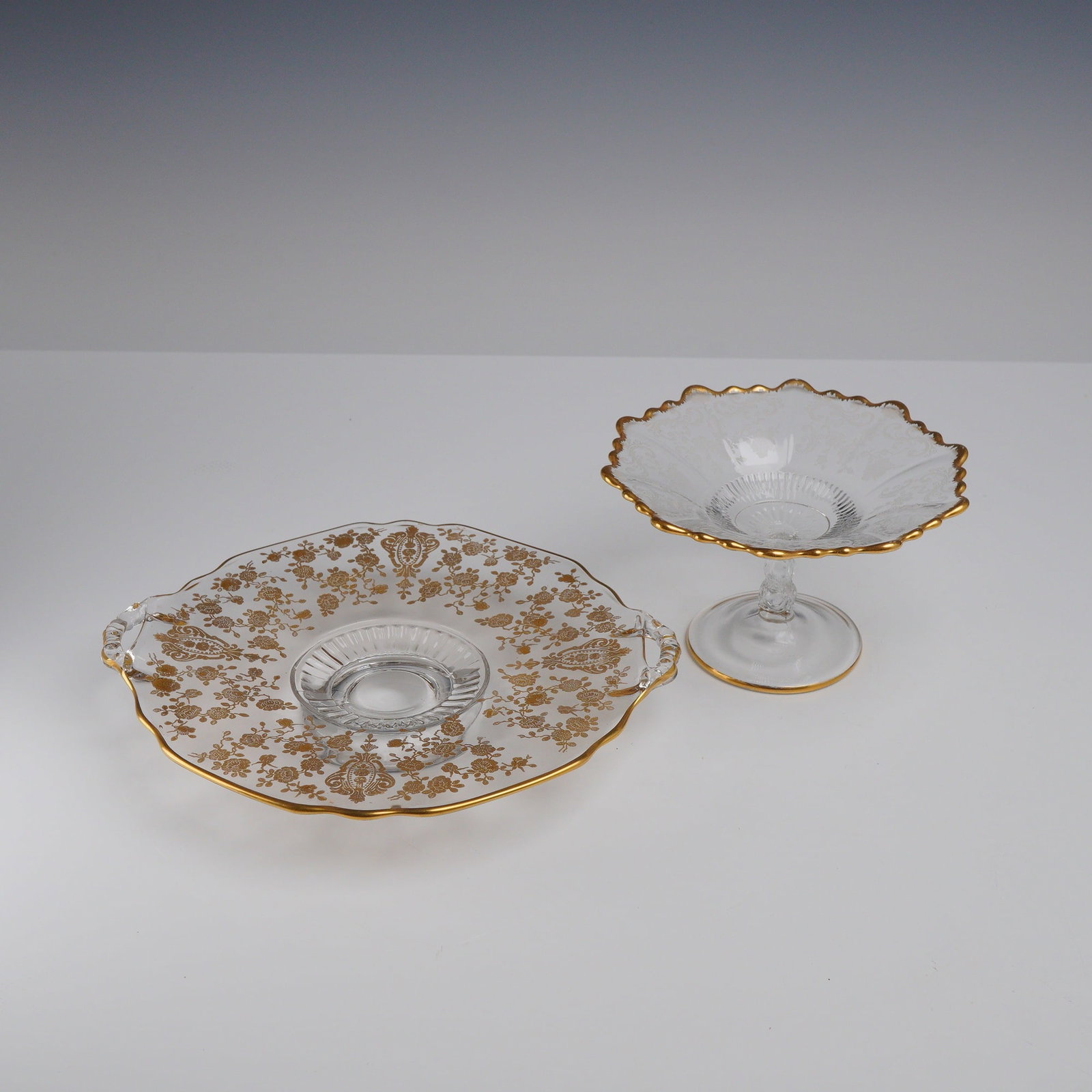 2pc Cambridge Glass Rose Point Gilded Glass Dishes: This lot consists of two pressed glass dishes from the American Elegant era, featuring intricate gold-encrusted and gold-gilt etched decorations. The first item is a circular handled serving plate by 