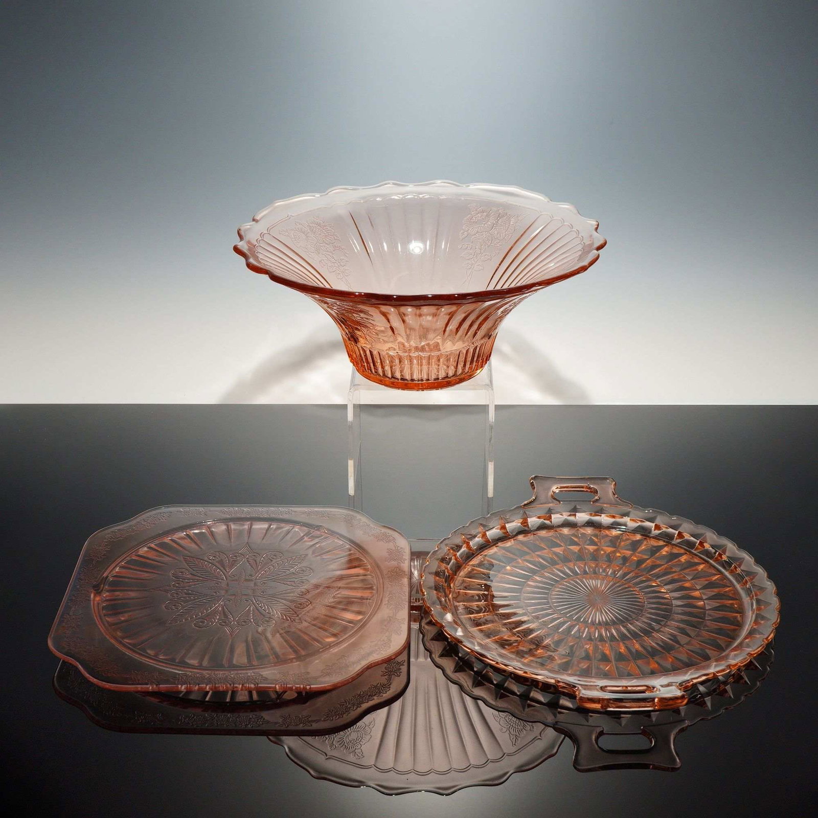 Three Pieces of Pink Depression Glass in Sharon, Windsor, and Patrician Patterns: This collection of pink depression glass consists of three serving pieces featuring patterns produced during the 1930s. The first item is a flared serving bowl in the Sharon pattern, frequently referr