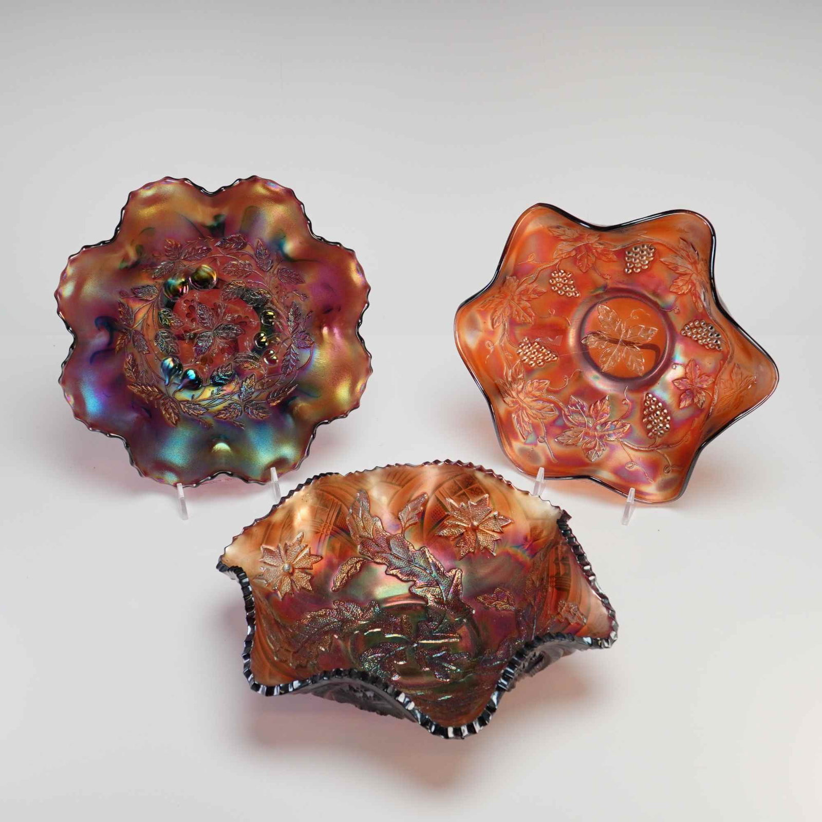 Three American Iridescent Carnival Glass Bowls in Three Fruits and Vintage Patterns: This lot features three pieces of American iridescent pressed carnival glass produced during the early 20th century. The first piece is an amethyst ruffled bowl with an interior molded pattern of cher