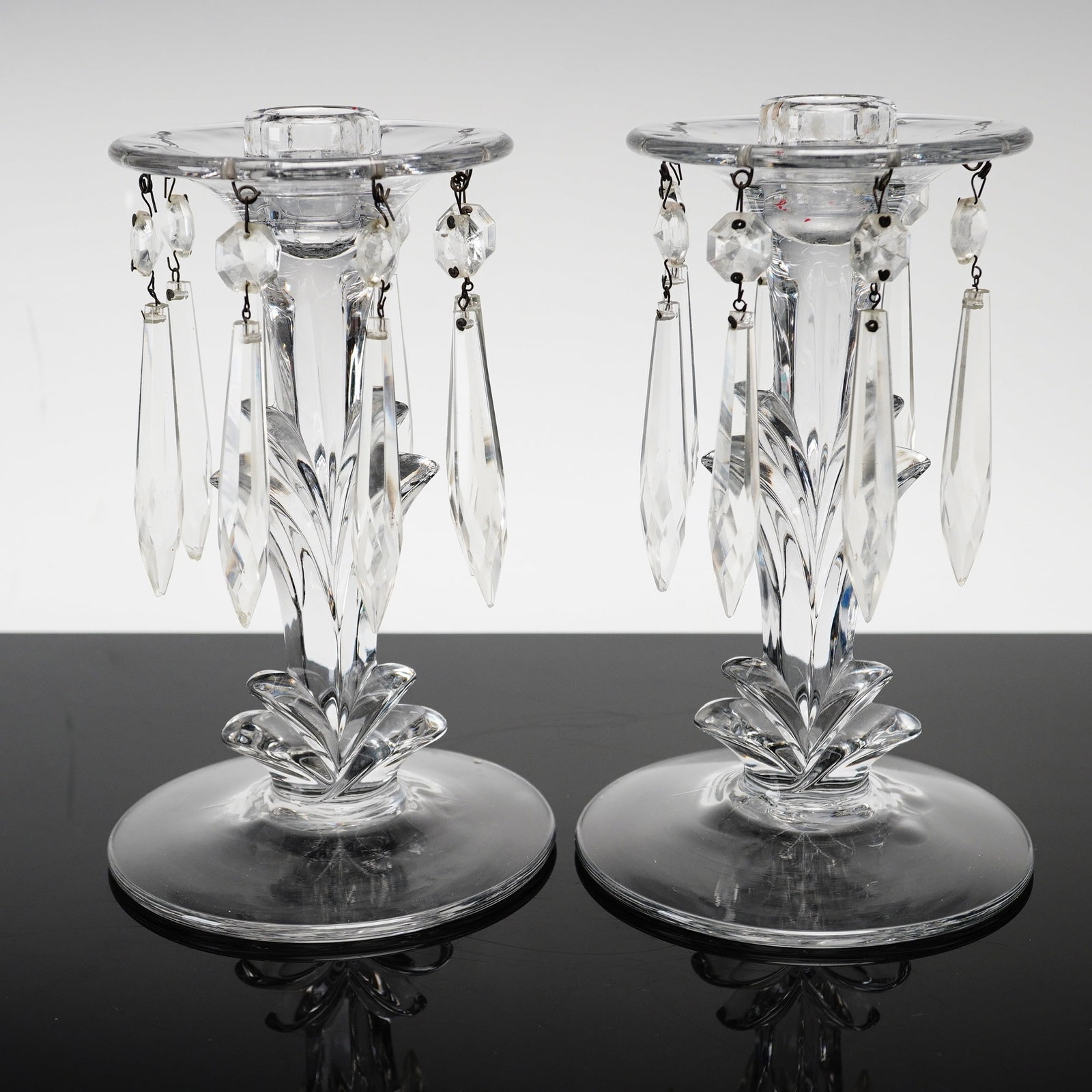 Pair of Cut Crystal Candlesticks with Hanging Prisms: This pair of clear cut crystal candlesticks features a central stem with stylized foliate cutting rising from a matching floral-form base. Each candlestick supports a wide, flat circular bobeche hung 