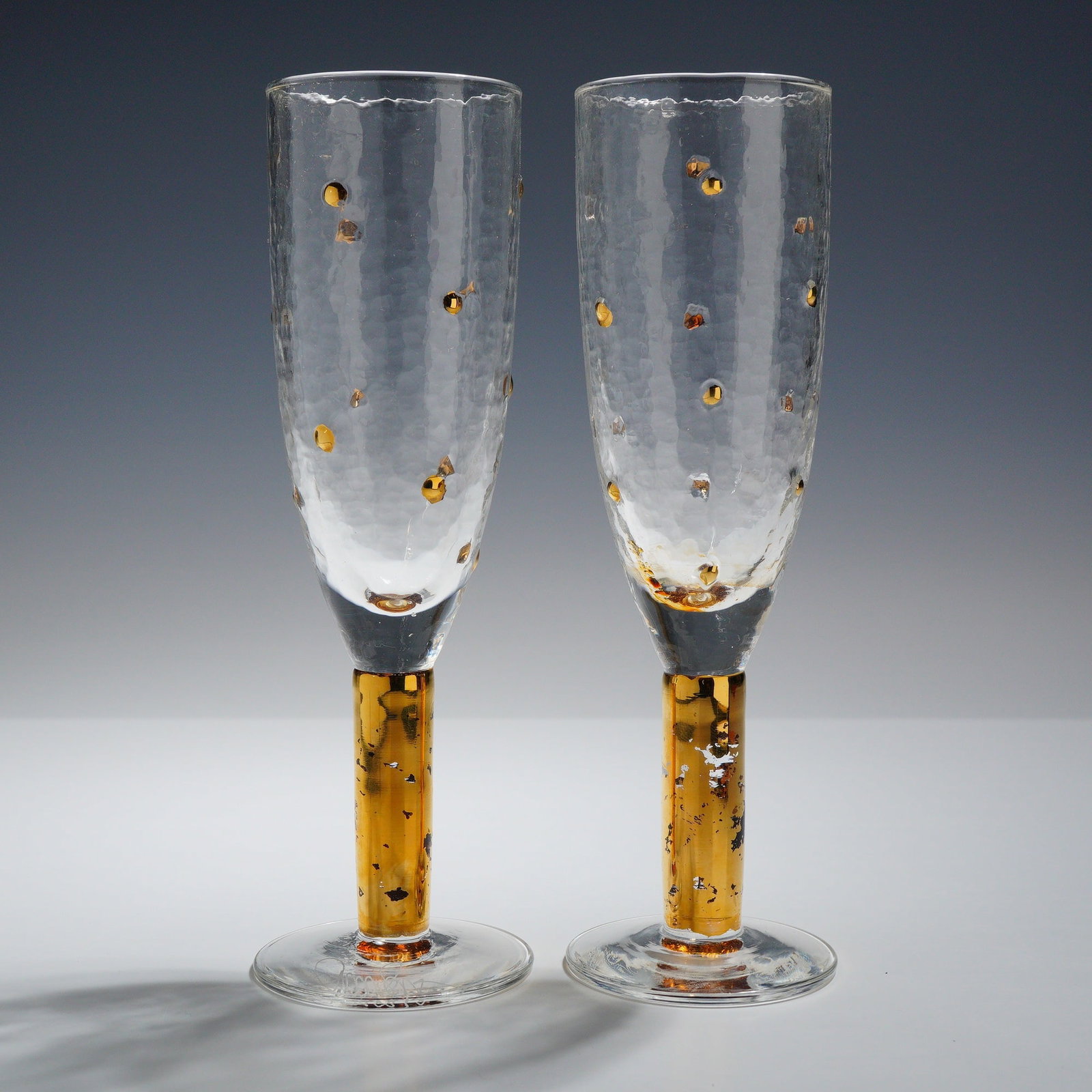 Pair of Smyers Hand-Blown Morocco Gold Champagne Flutes, Signed: This set of 2 x glasses is constructed from hand-blown clear glass featuring a bark-like optic texture on the bowls. The exterior of each bowl is decorated with multiple applied metallic gold-colored