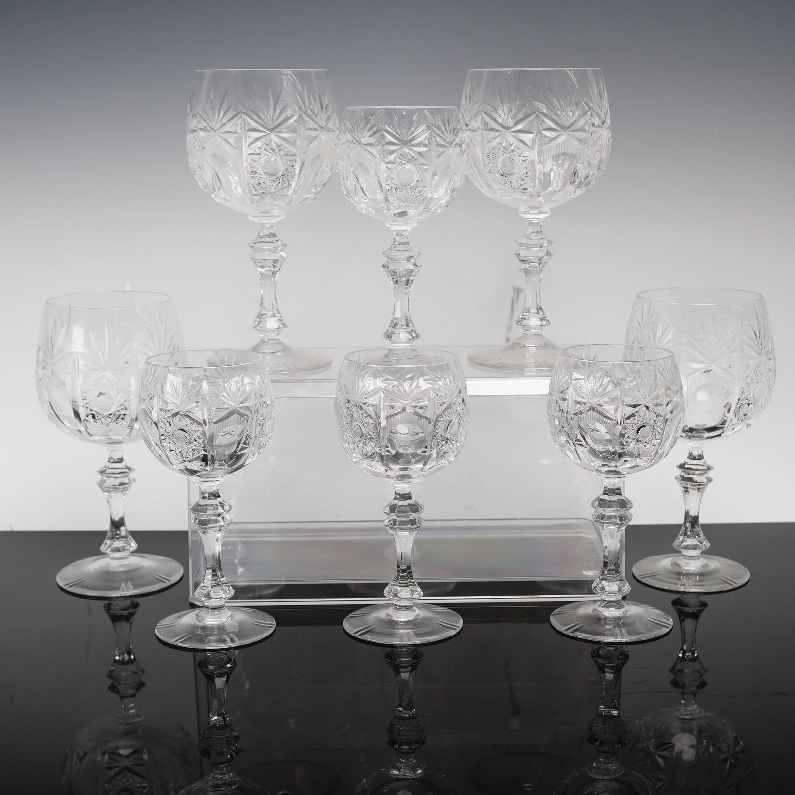 Set of Eight Russian Style Cut Crystal Wine Glasses: This set of eight cut lead crystal wine glasses is designed in a traditional Russian style, frequently attributed to makers such as Neman Glassworks. The collection is comprised of three larger