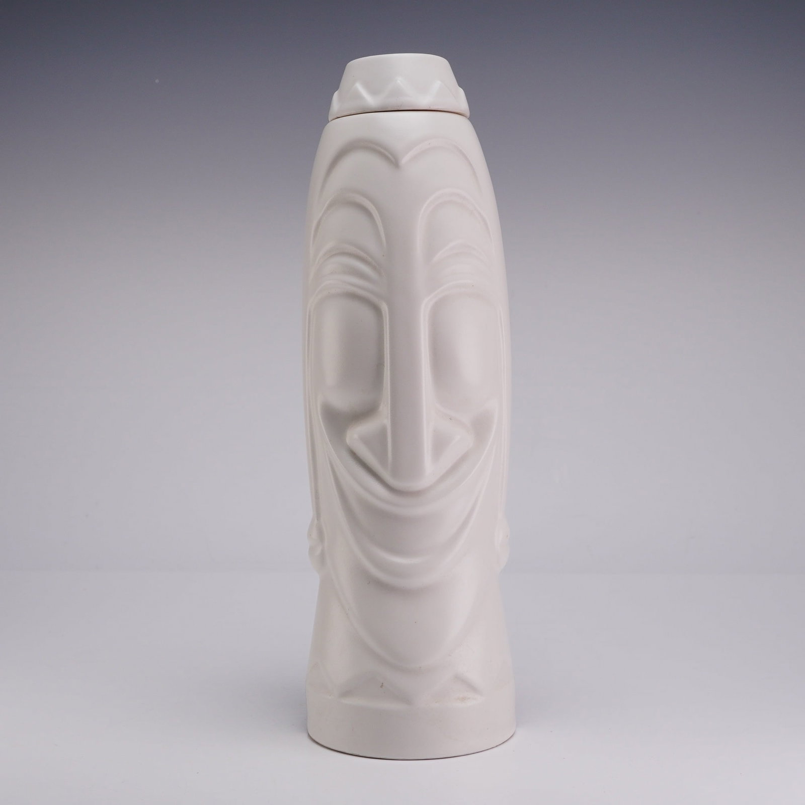 George Pisani Two-Face Contemporary Dual-Tone Decanter: This item is a contemporary Arrow Liqueurs George Pisani ceramic decanter constructed of porcelain with molded relief features. The exterior is decorated with a split-tone finish, featuring a matte bl