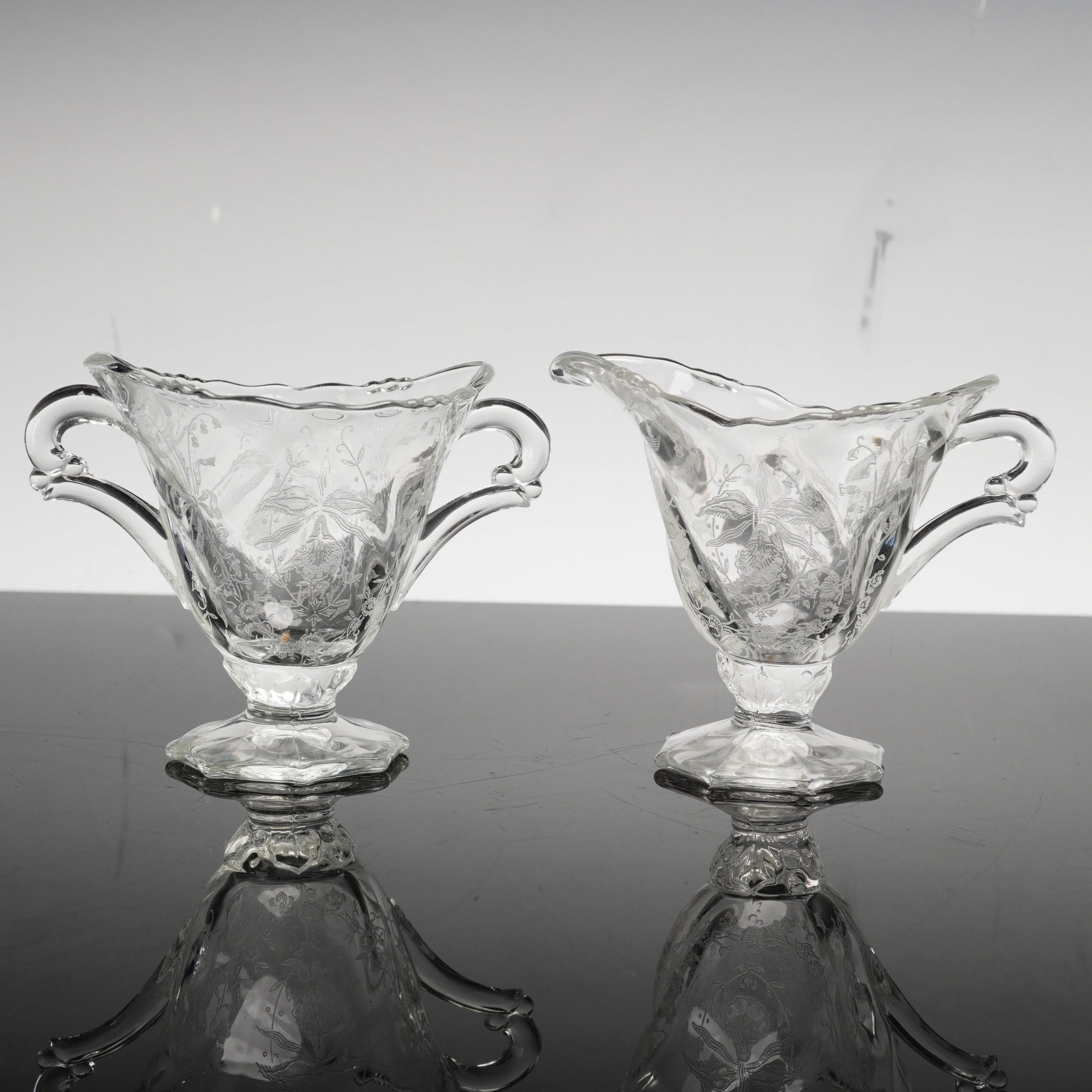 2 Pc Heisey Etched Clear Glass Footed Creamer and Sugar Bowl, Orchid: This pair of clear glass tablewares consists of a footed creamer and a matching two-handled open sugar bowl in the Orchid pattern by Heisey. The set is crafted from clear glass featuring an acid-etche