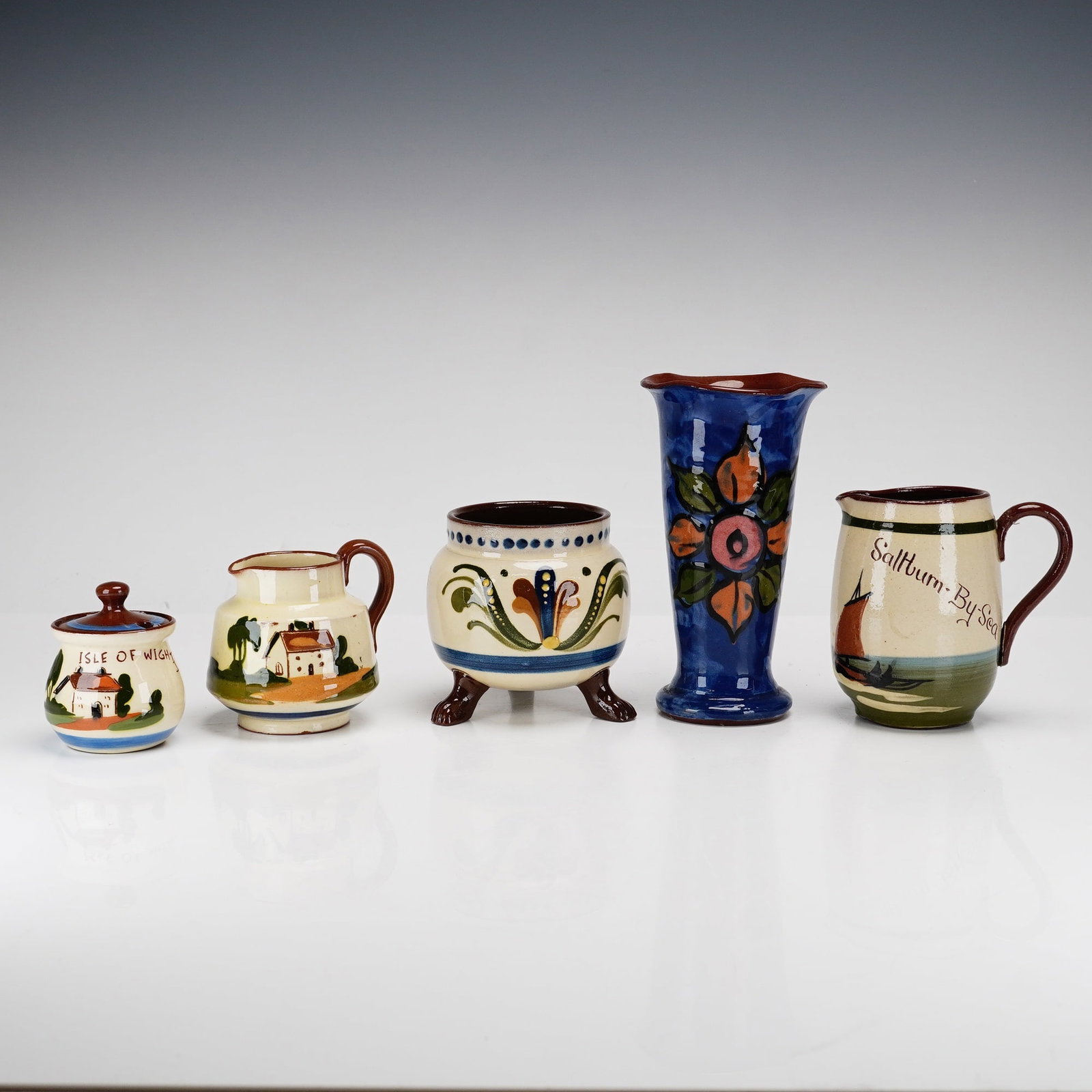 5pc English Watcombe Torquay Motto Pottery Ware: A collection of English Torquay Motto Ware, consisting of various slip-decorated red earthenware vessels. The group includes a small globular lidded pot with a knob finial, decorated with a cottage sc