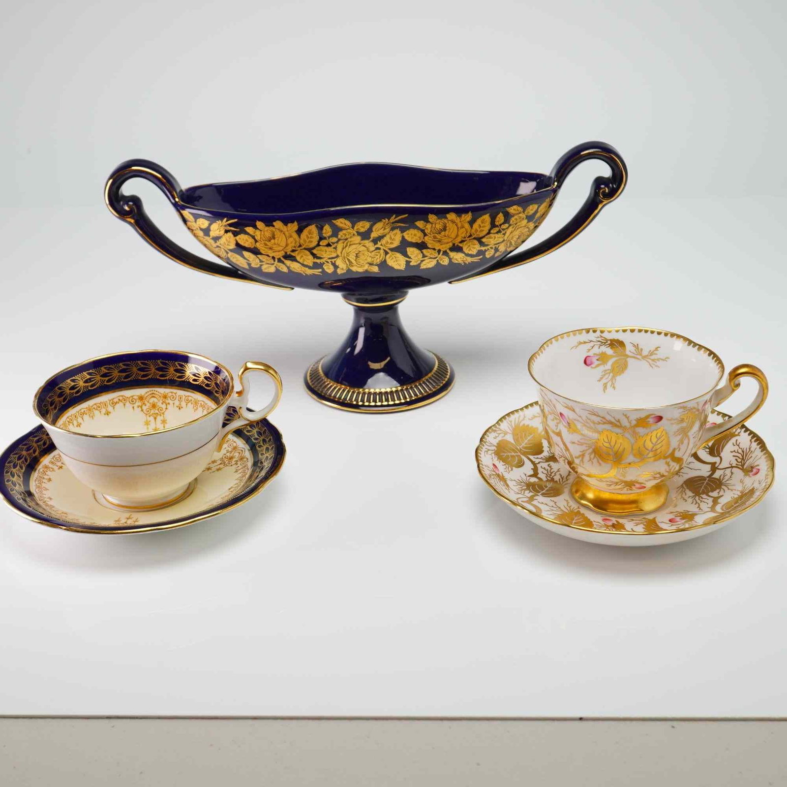 Five-piece Italian and English Tableware - Cups and Saucers with Compote Dish: Lot includes Cobalt Italian compote dish with floral gilt design; Royal Chelsea hand decorated Bone China cup and saucer with gilt leaf and vine design with pink bud accents; and Aynsley Bone China cu