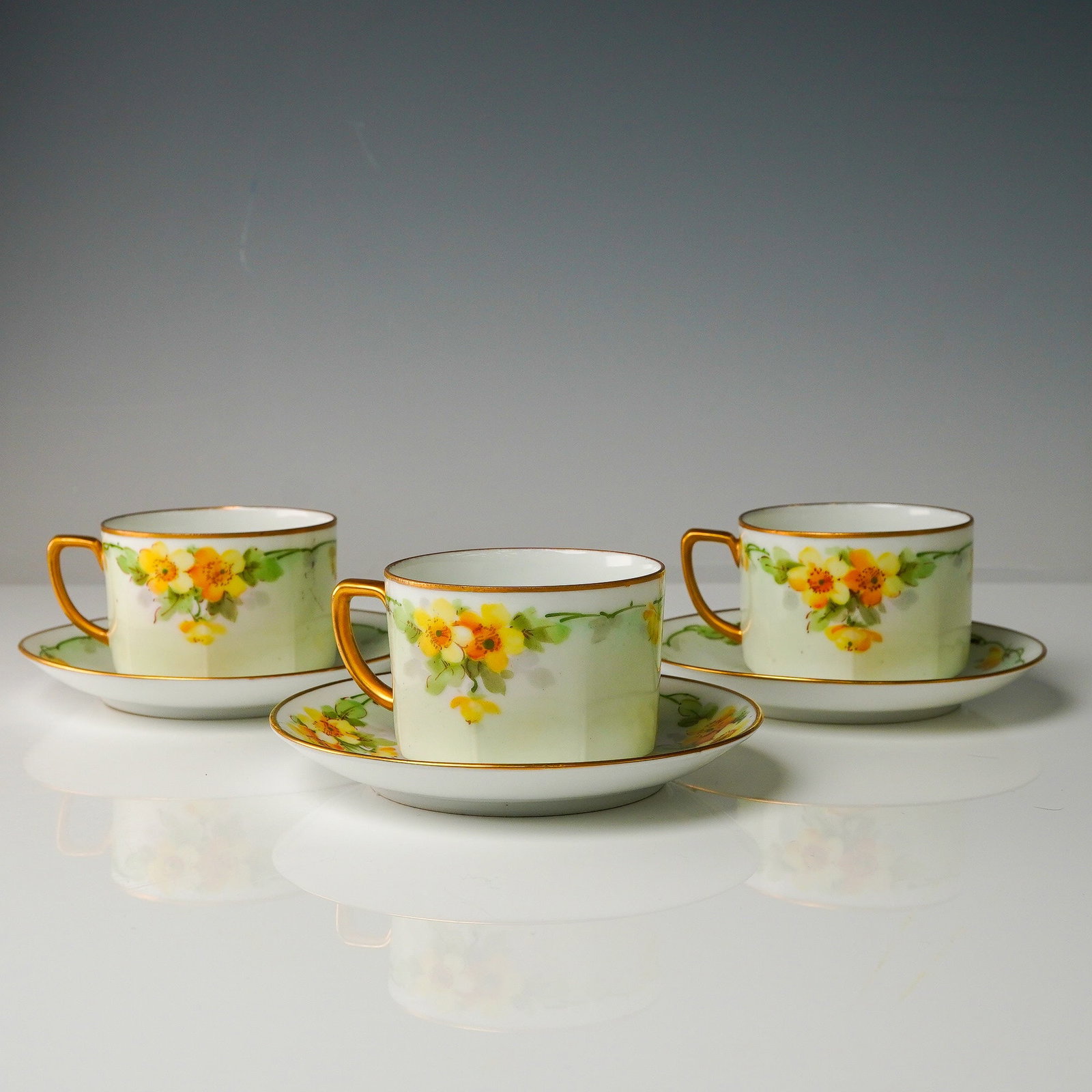 6pc Hand-Painted Yellow Floral Porcelain Cup & Saucer Trio, Austria: A charming 6-piece porcelain demitasse cups (3) and matching saucers (3), each delicately hand-painted with yellow and orange blossoms, leafy green garlands, and highlighted with gilt detailing. The c