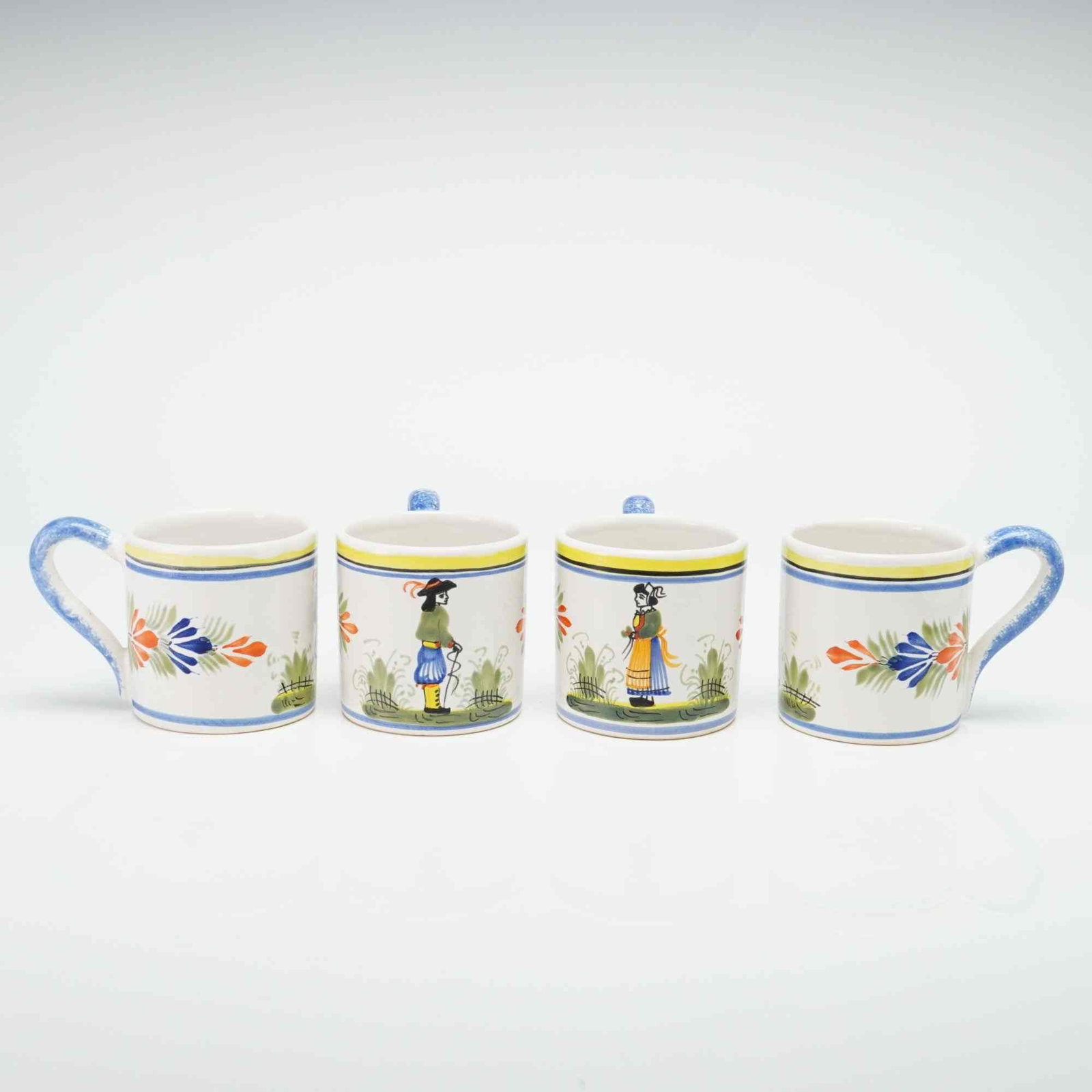 Set of Four HB-HenRiot Quimper Hand-Painted Ceramic Mugs: This collection of hand-painted earthenware mugs is produced by the HB-HenRiot factory in Quimper, France. The pieces are decorated in the traditional Breton folk style. A portion of the set depicts a