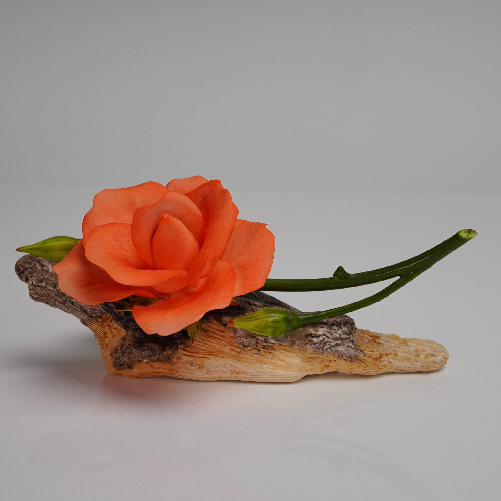 Boehm Bone Porcelain Coral Rose Sculpture 200-55-S: A single naturalistic floral sculpture crafted from Boehm Bone Porcelain, model number 200-55-S. The piece depicts an open rose in vibrant coral/orange hues, accompanied by a thorny green stem and two