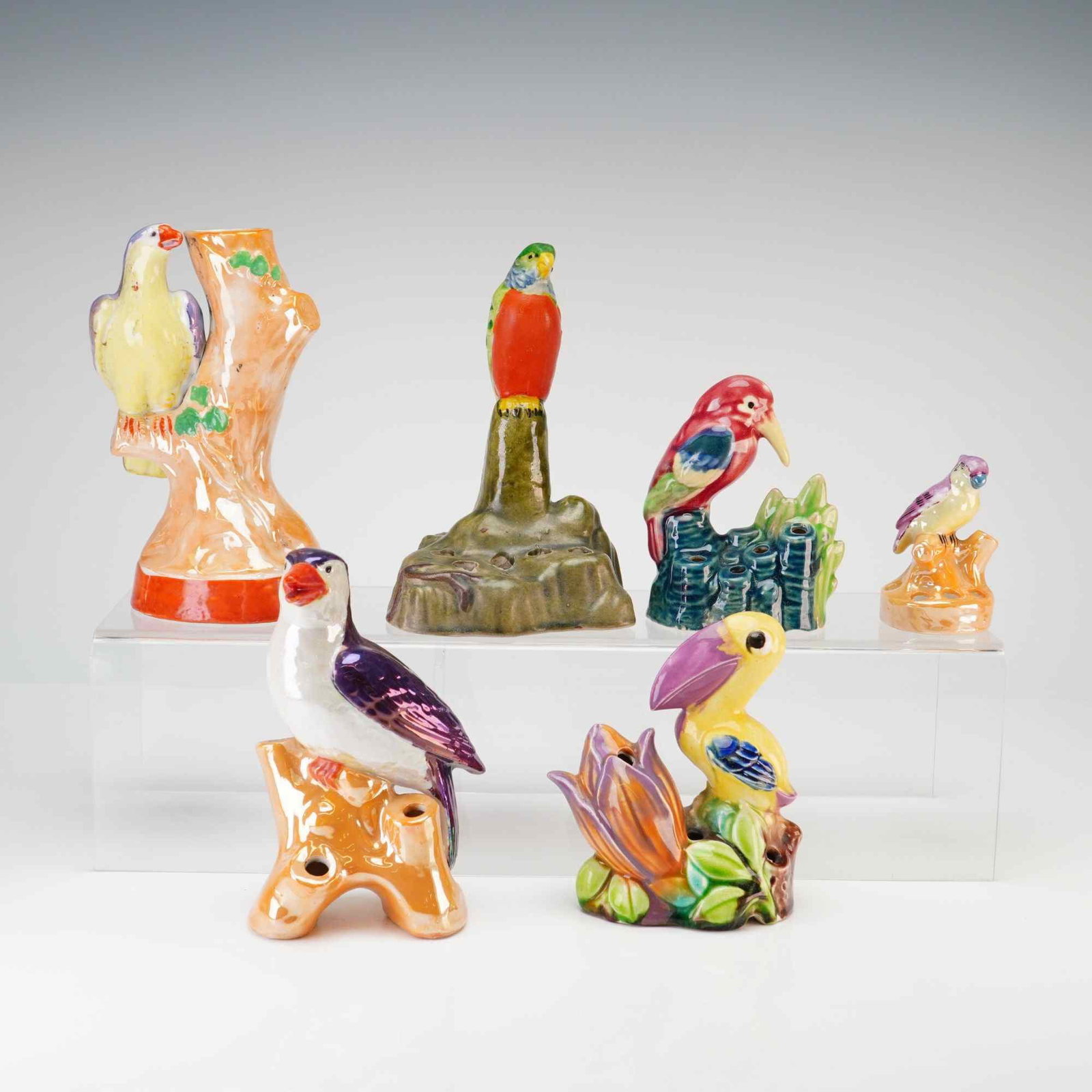Collection of Six Japanese Lusterware Tropical Bird Flower Frogs: This collection consists of several Japanese ceramic figurines depicting various tropical and exotic birds, including a toucan, parrots, and a kingfisher-style species. The pieces are primarily design