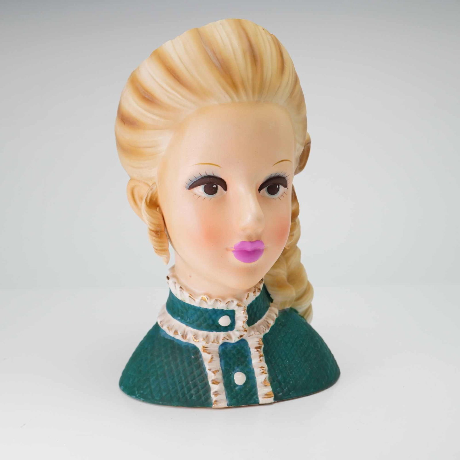 Mid-Century Ceramic Lady Head Vase w/ Teal Quilted Jacket & Blonde Braid: This mid-century lady head vase is constructed from glazed earthenware with a matte bisque finish applied to the skin tones. The figure depicts a young woman with blonde hair styled in a side-swept br