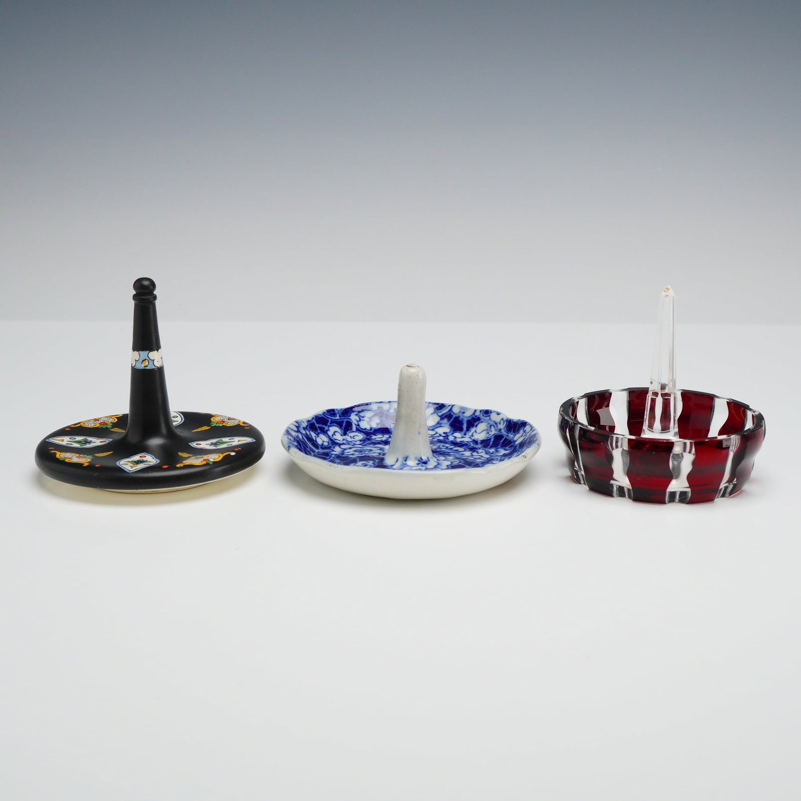 Three Antique Ring Tree Dishes Including Ruby Flash Glass and English Blue Chintz: This lot consists of three antique ring tree dishes in various materials and decorative styles. The first item is a black ceramic ring tree with a matte finish, featuring hand-painted colorful Art Dec